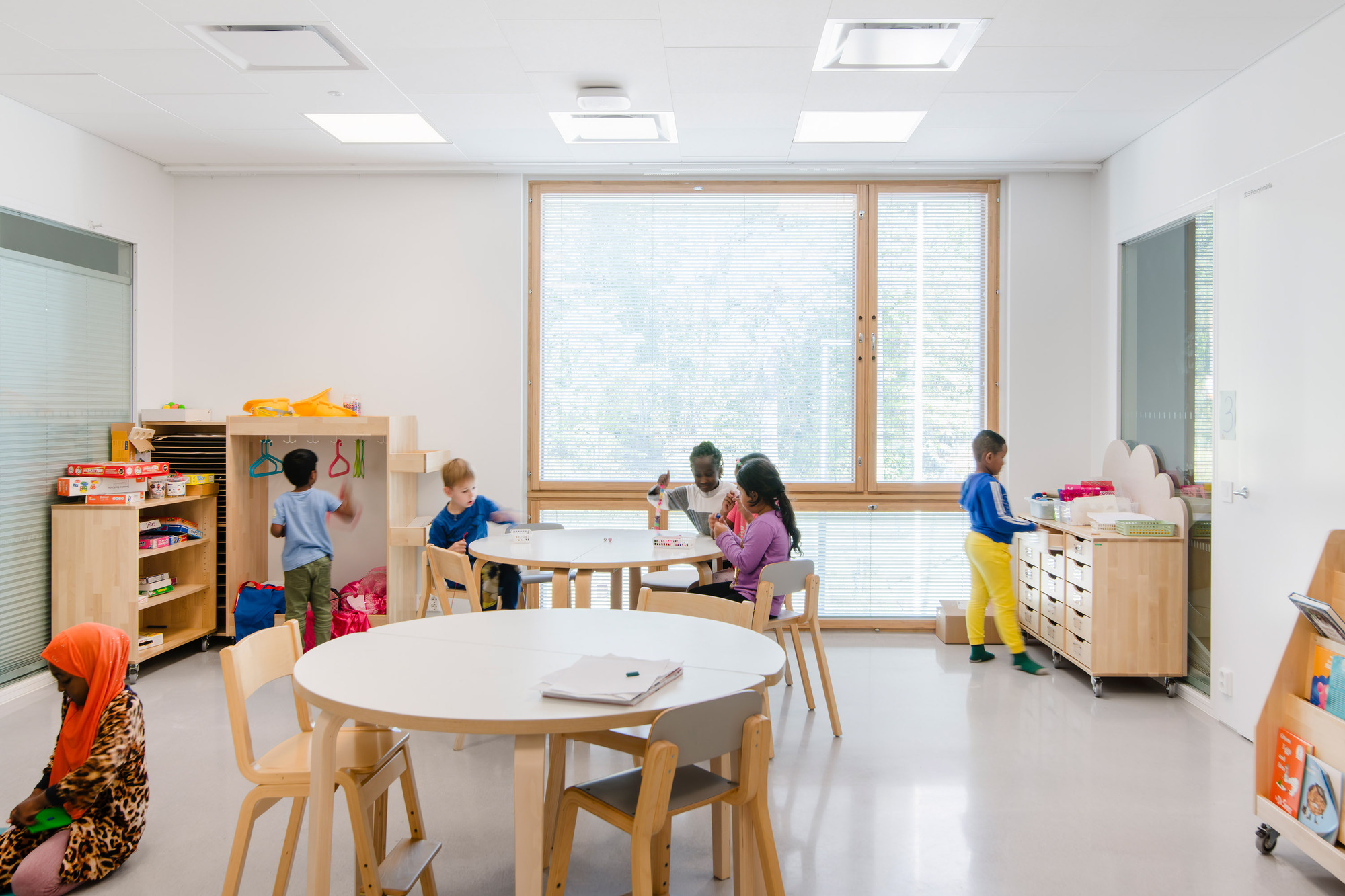 White classroom with timber-framed window, ceiling skylights and children working at low tables