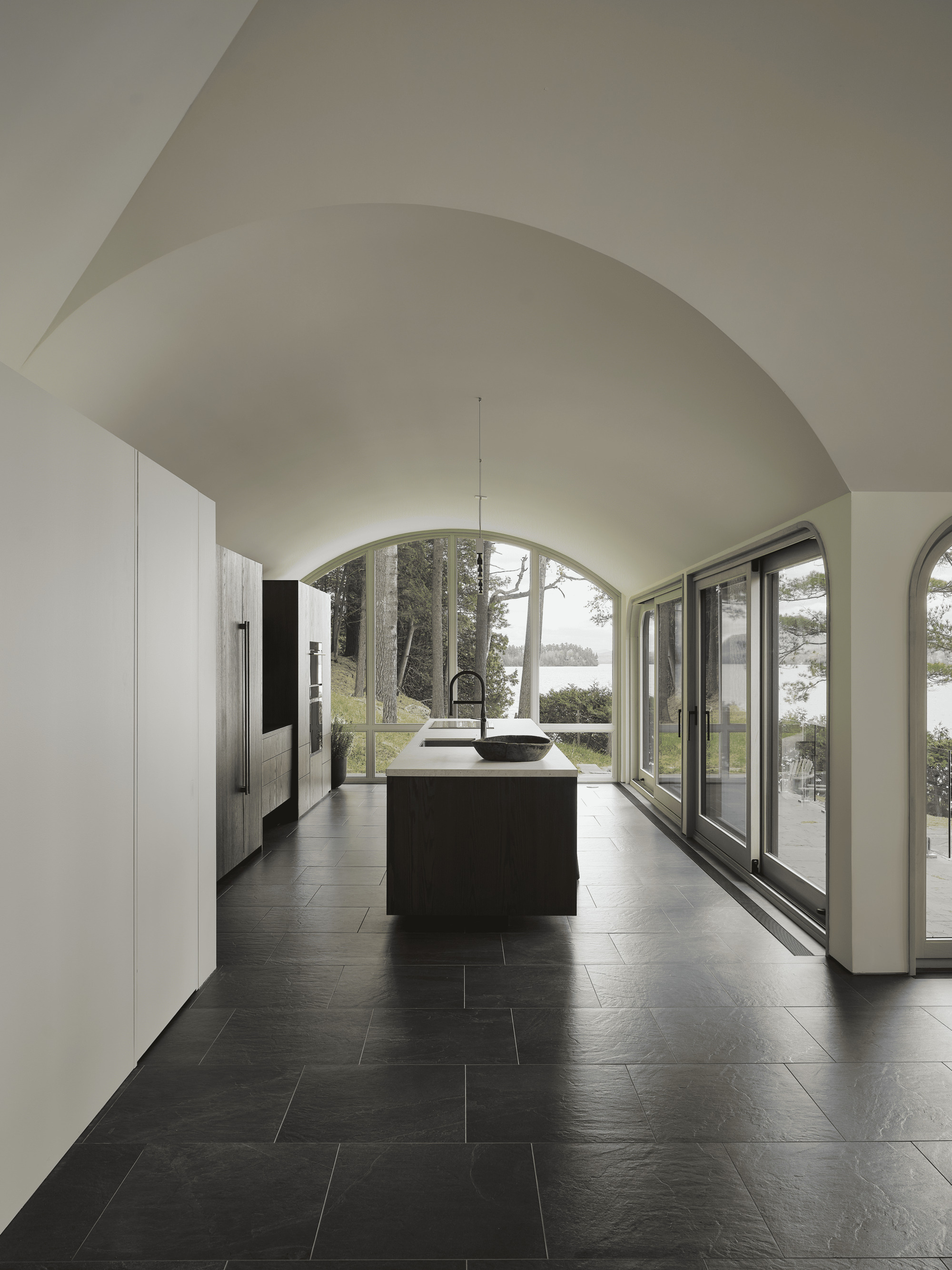 Vaulted kitchen with dark stone floor and arched glazing overlooking the lake