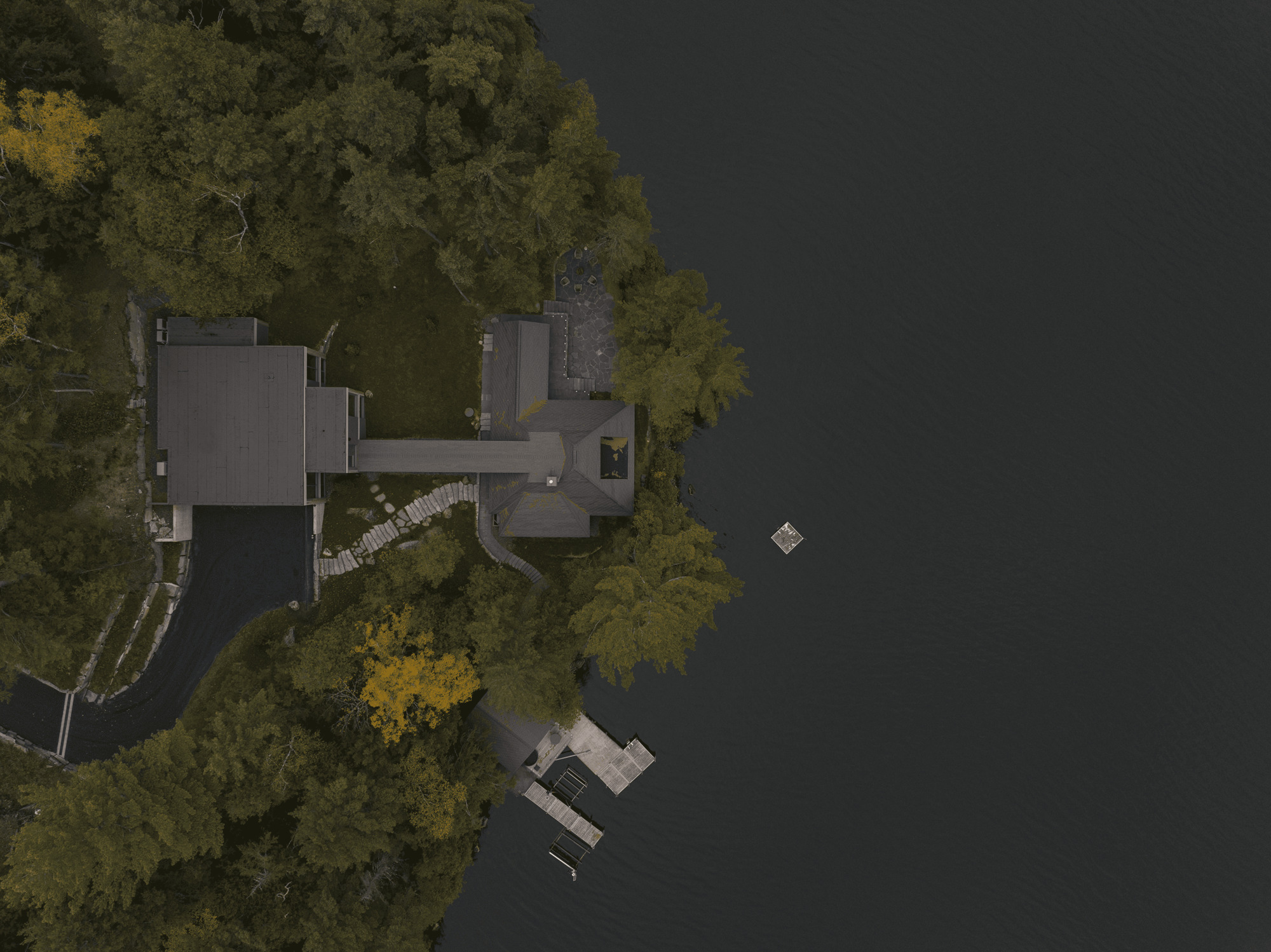 Drone view of the compound on the wooded shoreline with dock in dark water