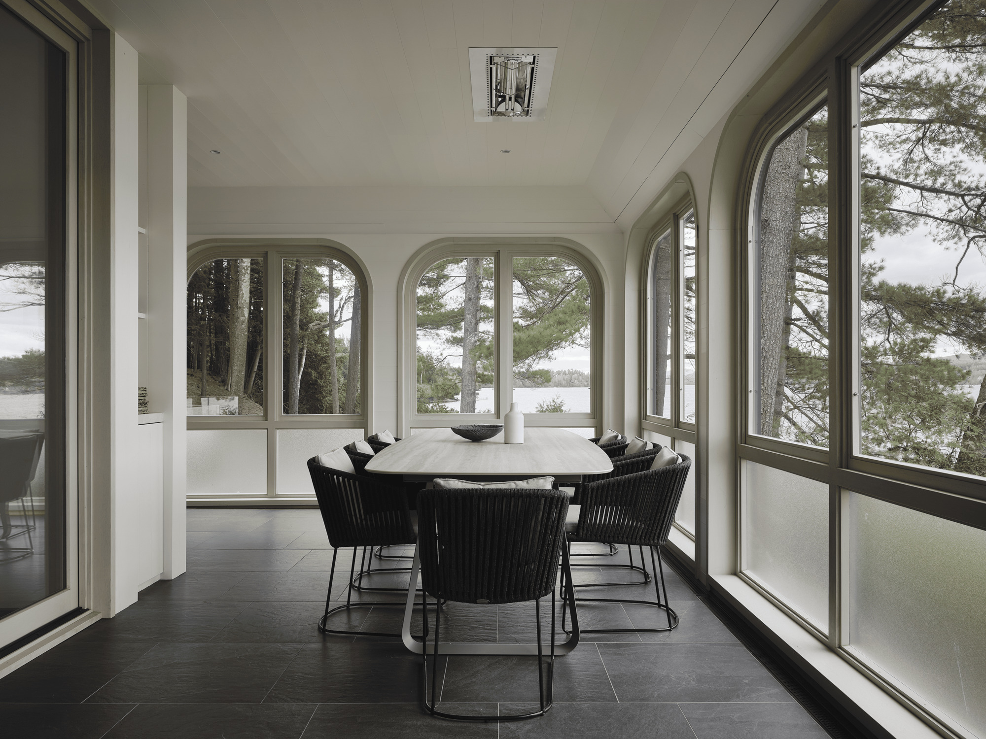 Dining room with arched window bays overlooking the lake through pine forest in overcast light