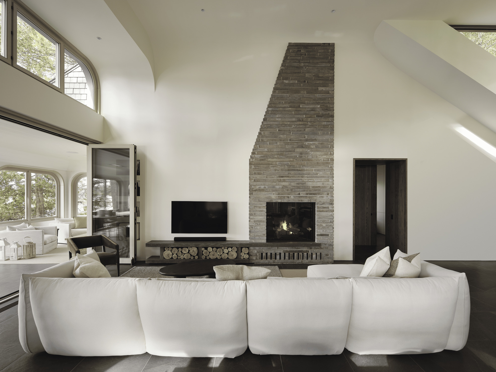 Vaulted living room with stacked brick fireplace, arched clerestory windows, and firewood storage niche