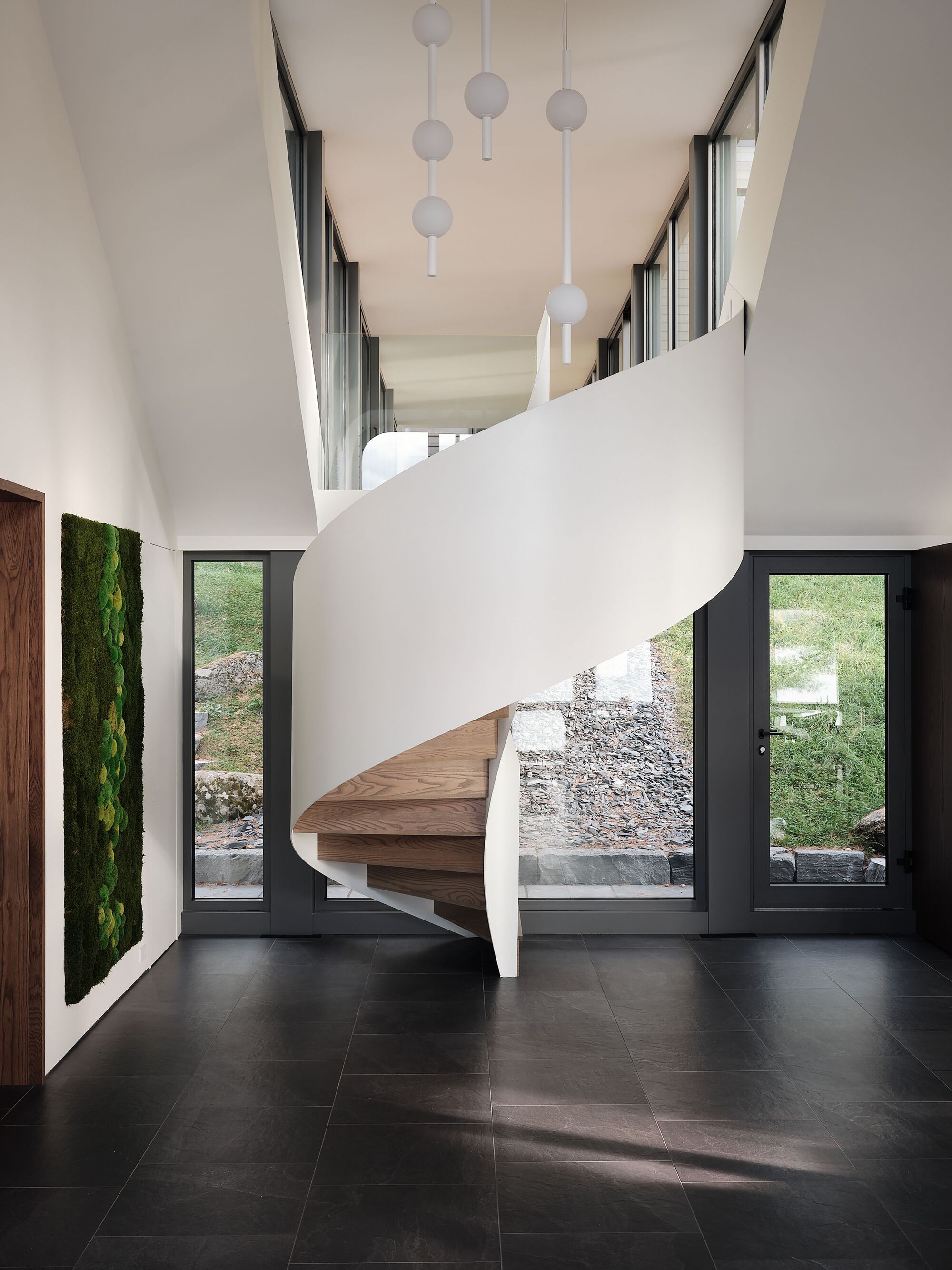 Helical staircase with timber treads and white balustrade beneath suspended globe pendants