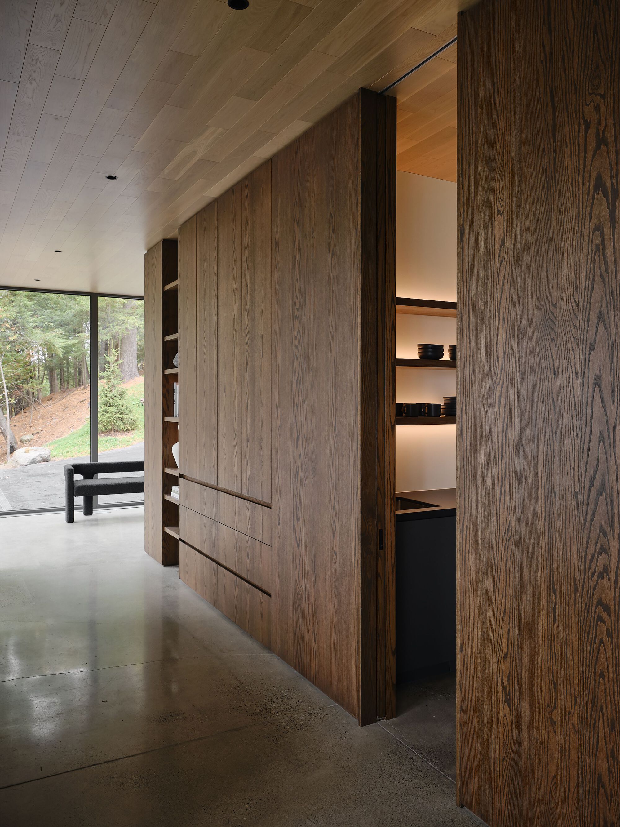 Built-in timber cabinetry with sliding panels and illuminated shelving along a polished concrete floor