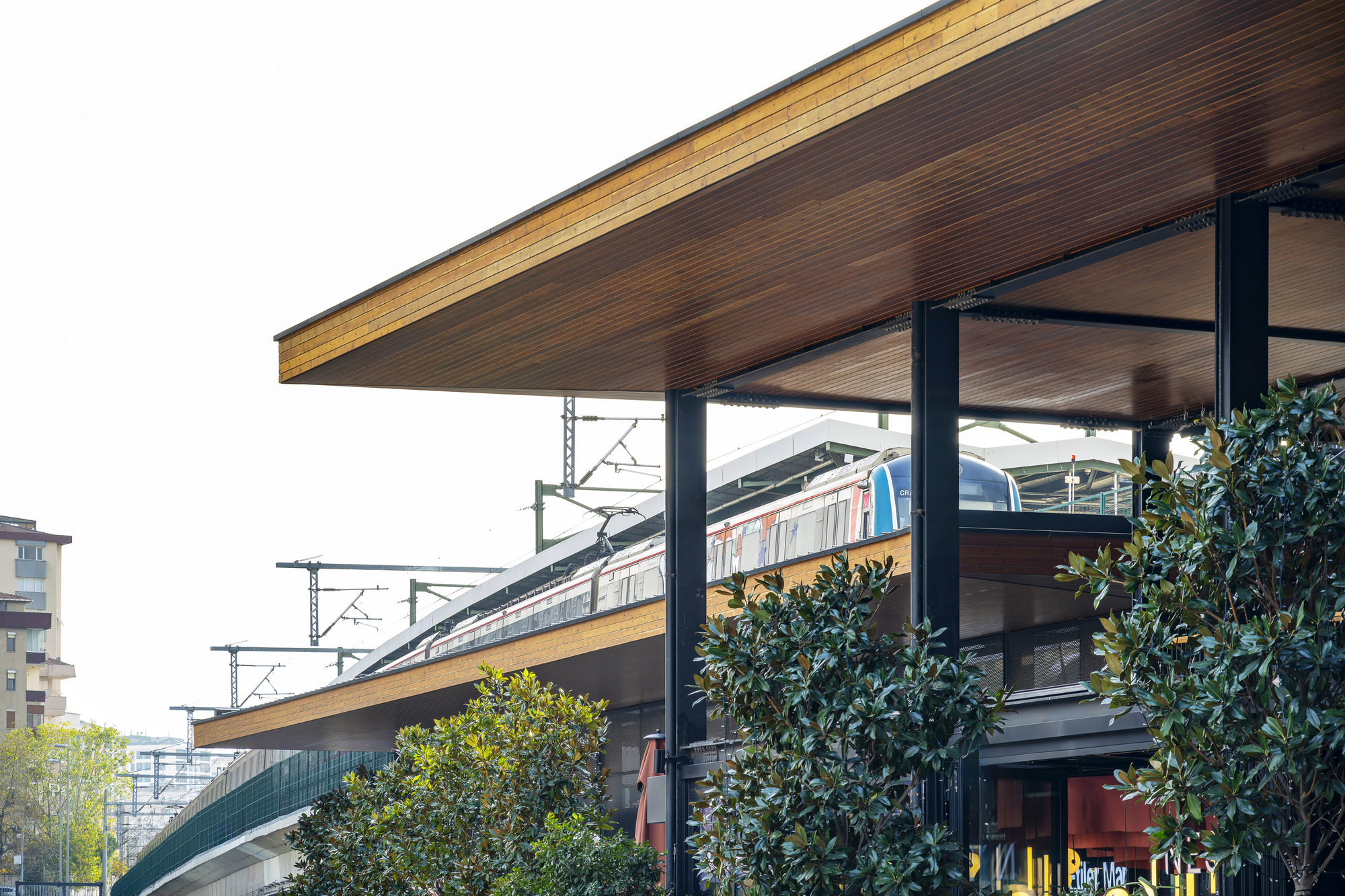 Cantilevered timber soffit roof supported by steel columns above the transit platform with train passing