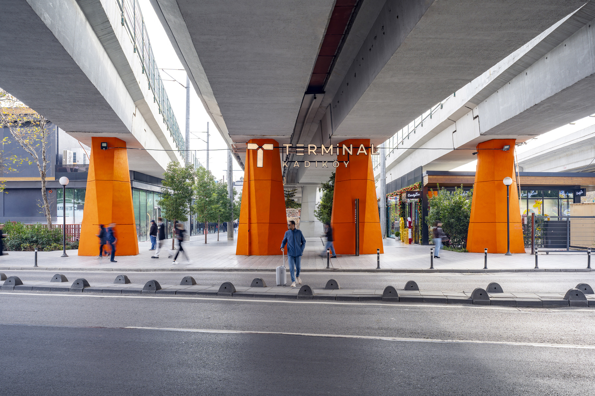Street view of orange-clad steel columns supporting concrete viaduct with pedestrians crossing at grade