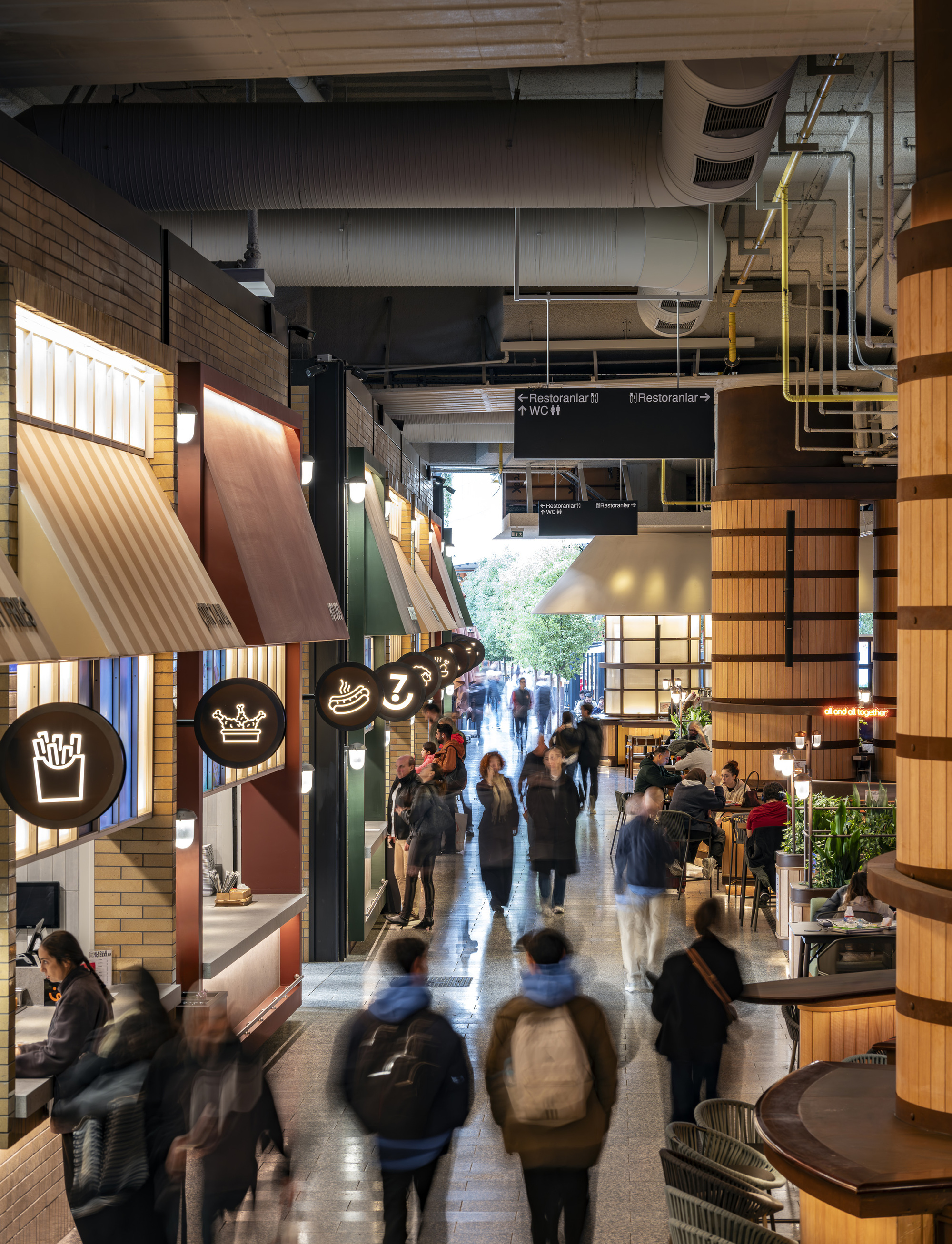 Interior passage with tiled food kiosks under exposed ductwork as pedestrians move through the corridor
