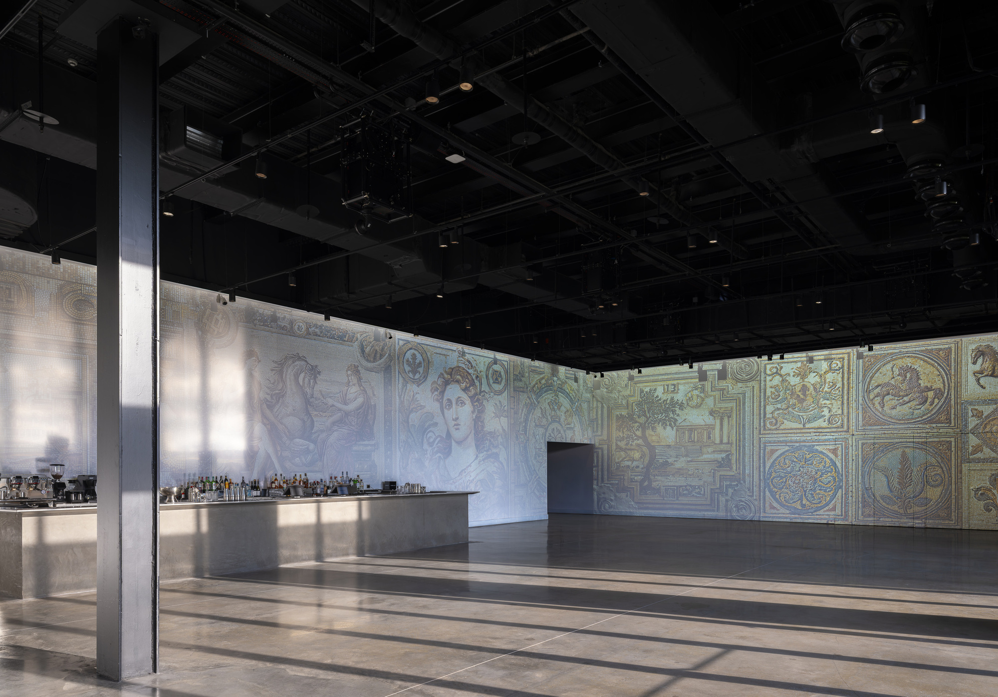 Open event hall with black exposed ceiling, decorative fresco walls, and polished floor reflecting overhead lighting