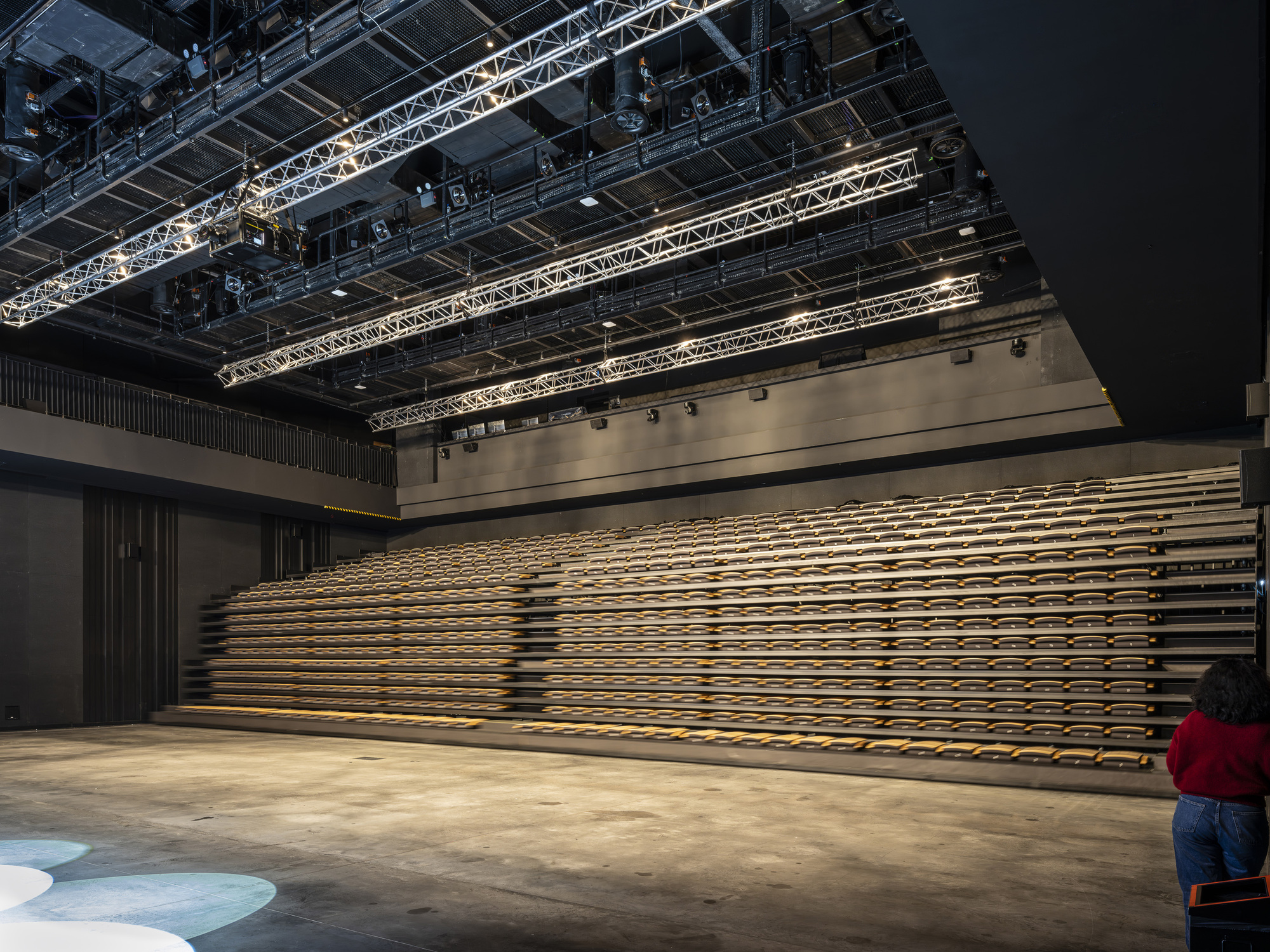 Retractable timber bleacher seating along the wall beneath exposed lighting truss and rigging infrastructure