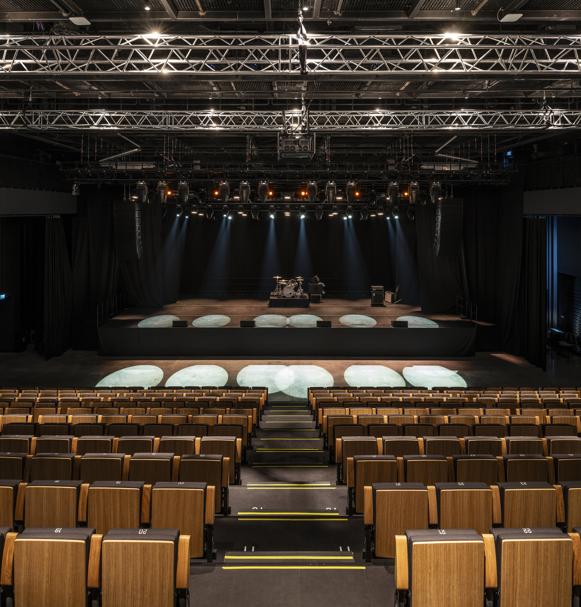 View from auditorium toward stage with timber seats, circular stage platforms and theatrical lighting above