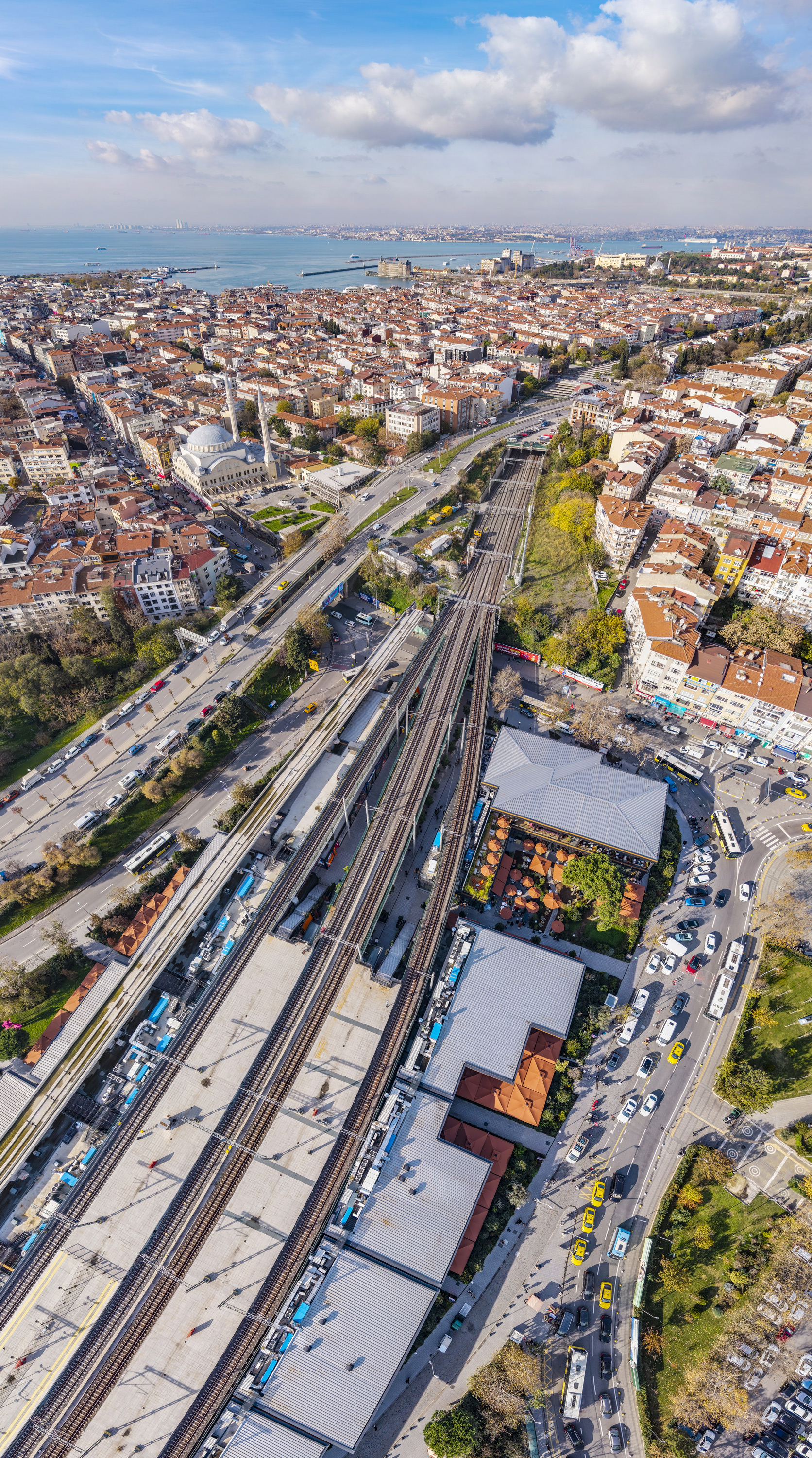 Aerial view of railway station complex with multiple platforms alongside residential neighborhoods and coastal bay
