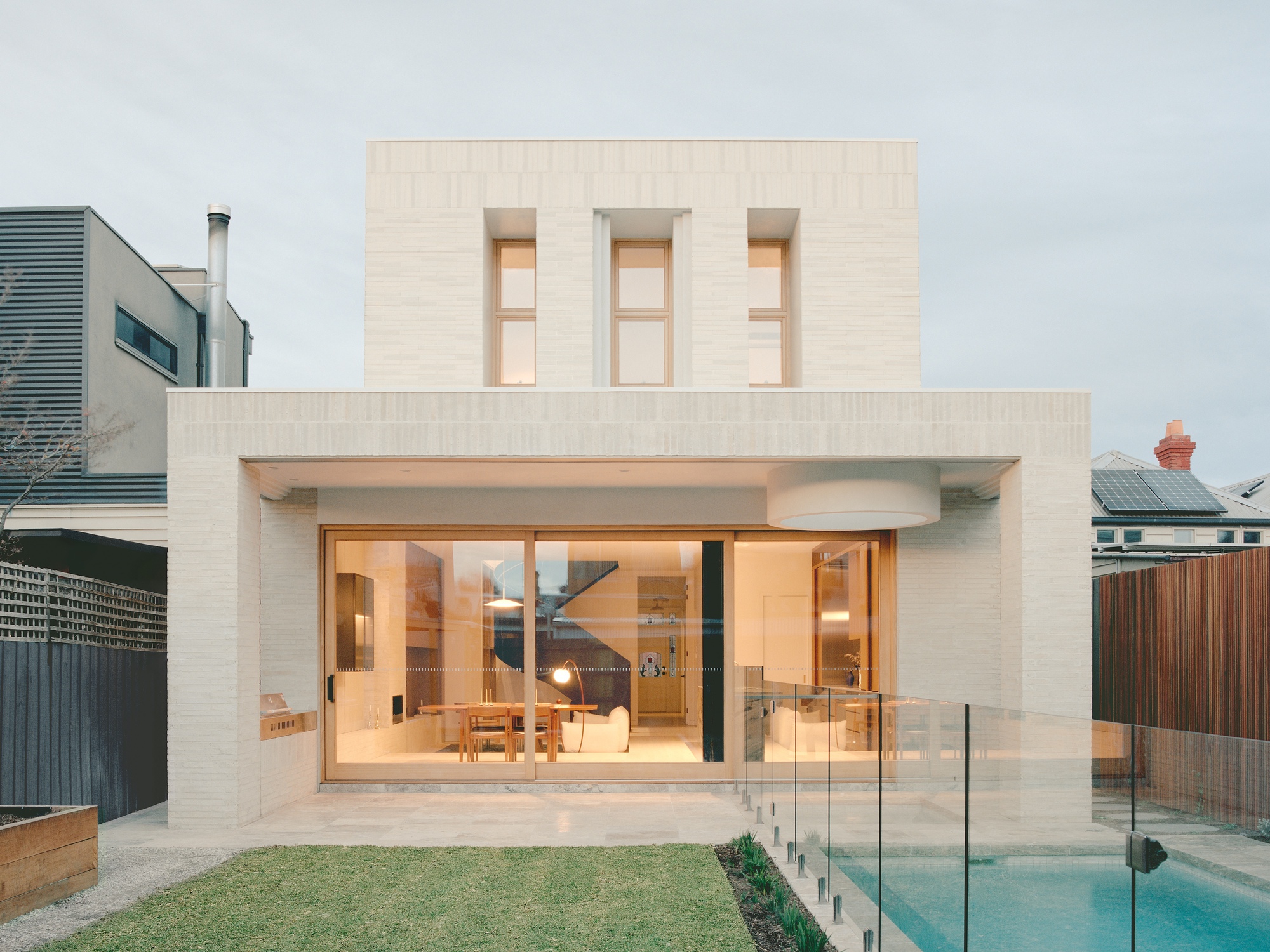 Rear facade with pale brick, recessed glazed doors, three upper windows, and adjacent pool with glass balustrade
