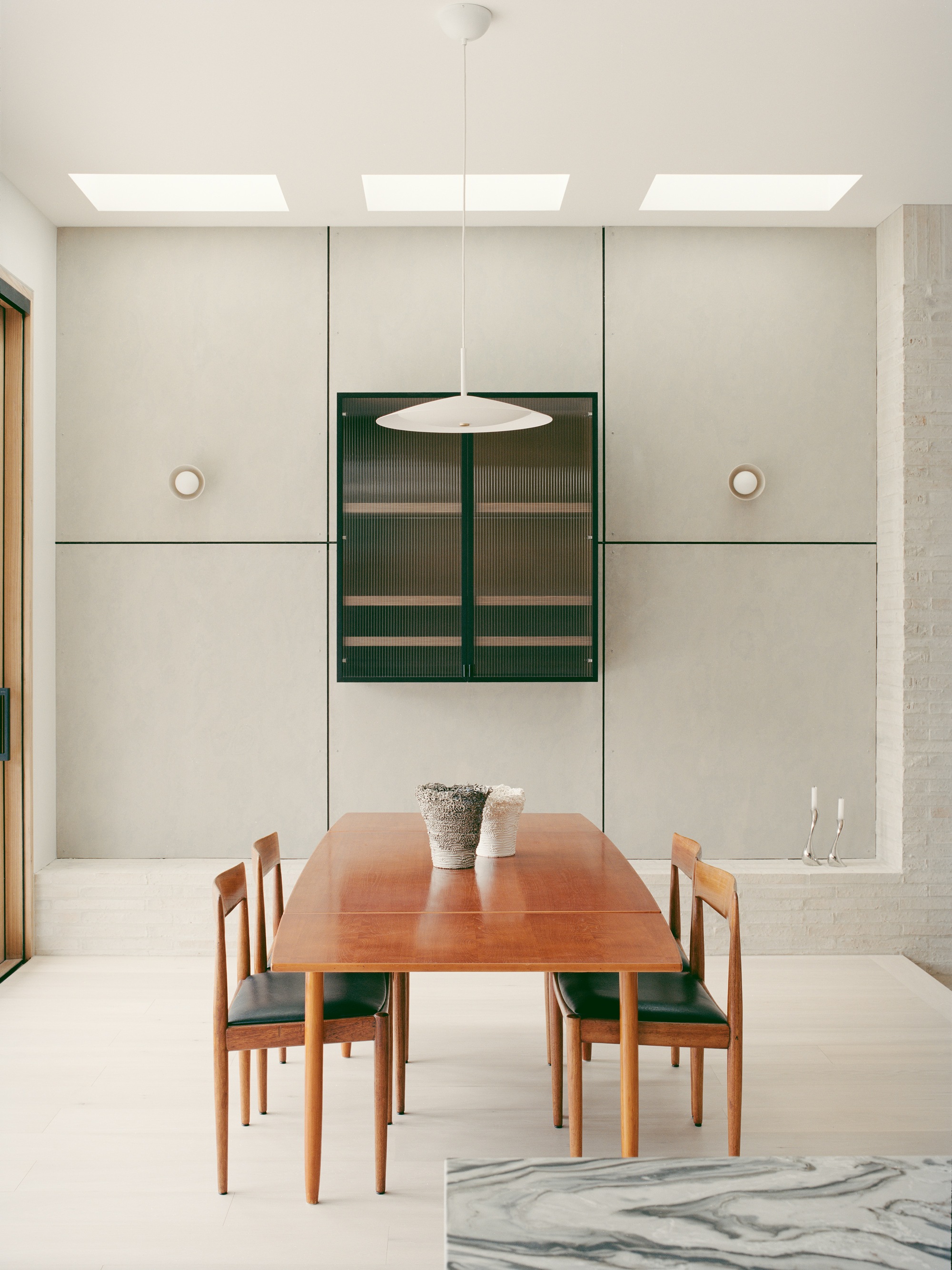 Dining room with timber table and green upholstered chairs below three skylights and pendant light fixture