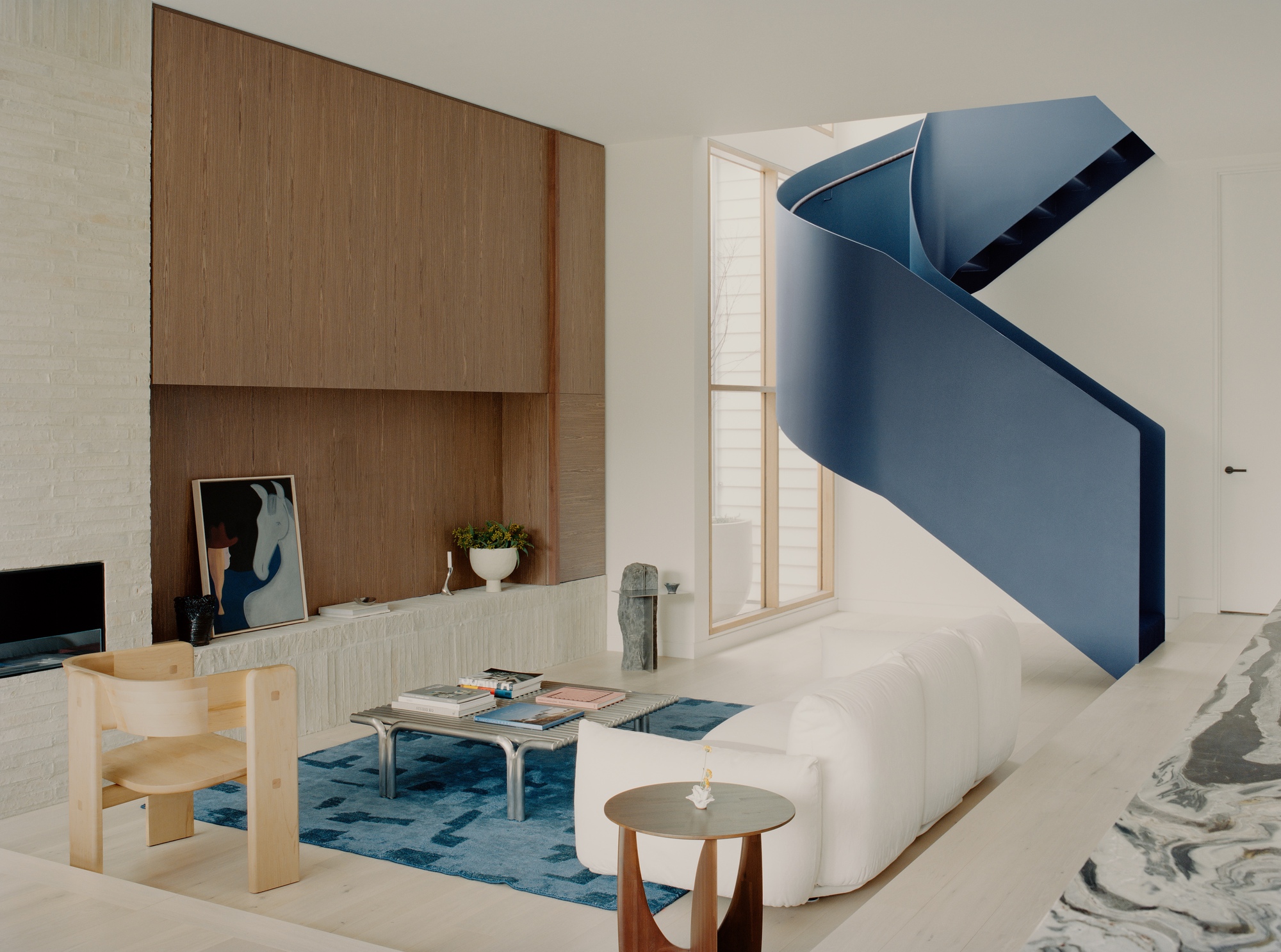 Blue folded metal staircase ascending through a double-height living space with timber joinery