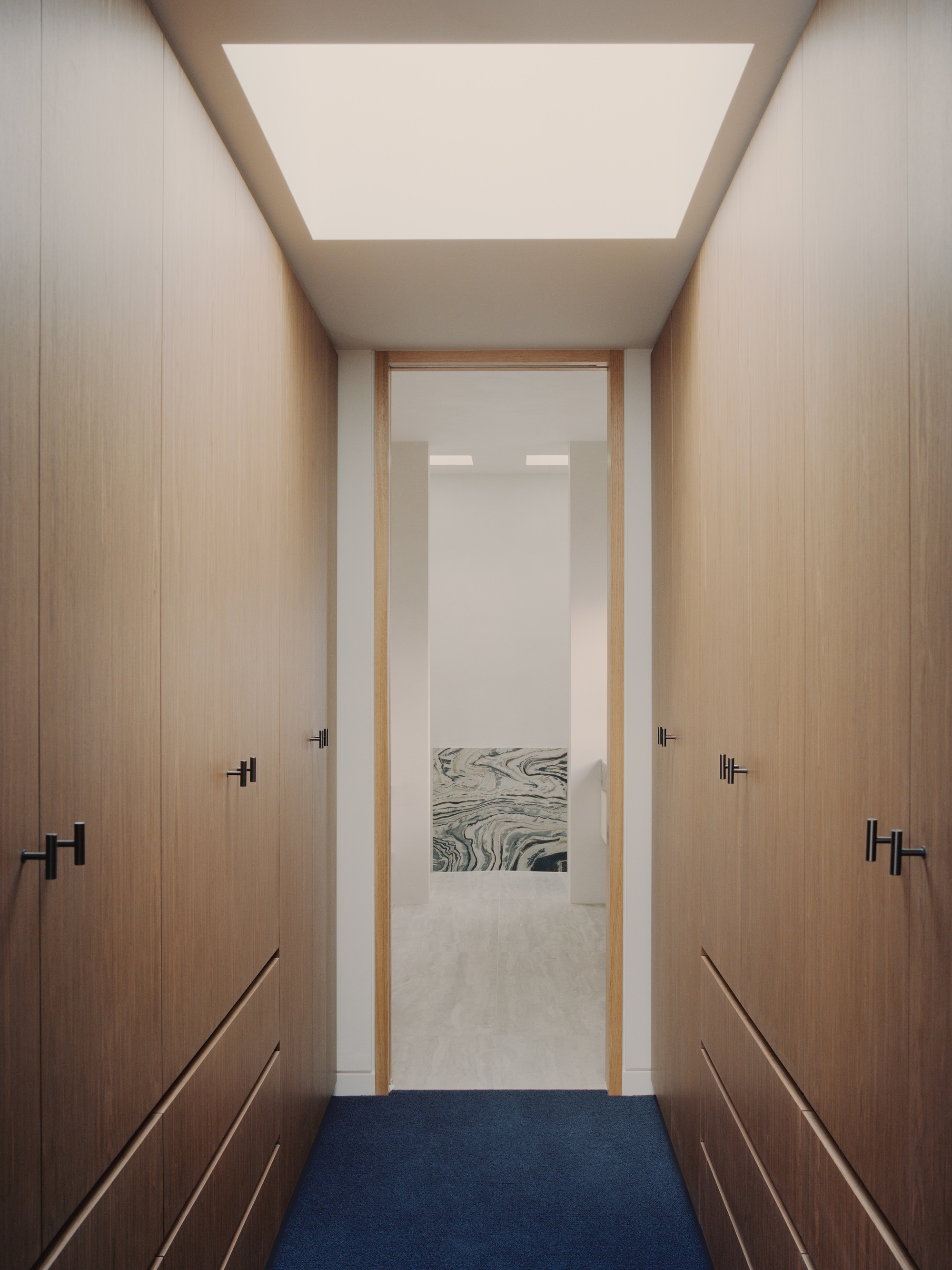 Narrow dressing corridor with timber wardrobes flanking a doorway framed by large ceiling skylight