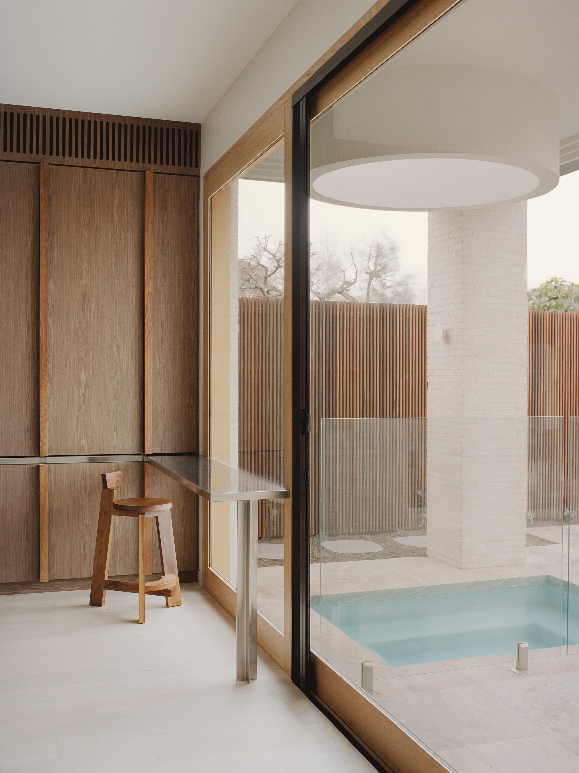 Interior view through timber-framed glazing to courtyard bathing space with vertical wood slat screens