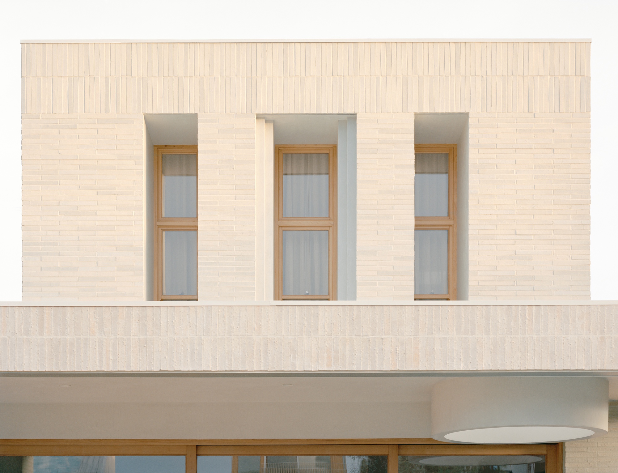 Facade detail showing three tall timber-framed windows set into pale brick wall with vertical bond