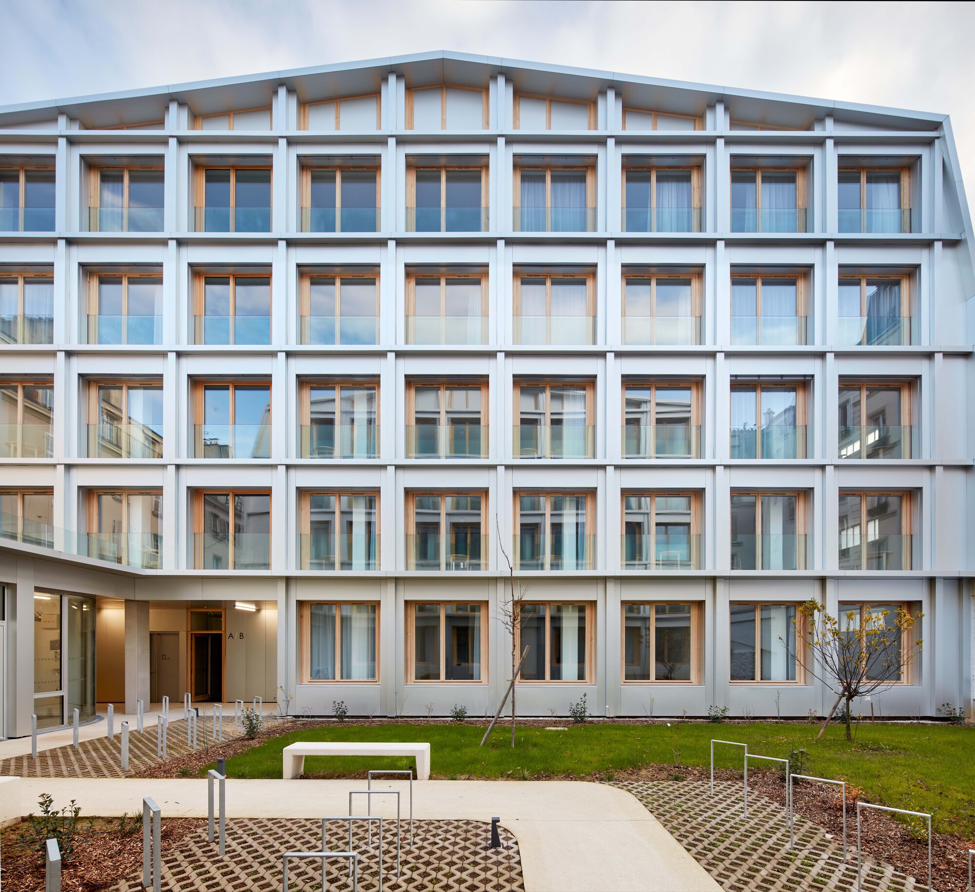 Five-storey courtyard facade with white structural frame and timber-framed windows under overcast sky