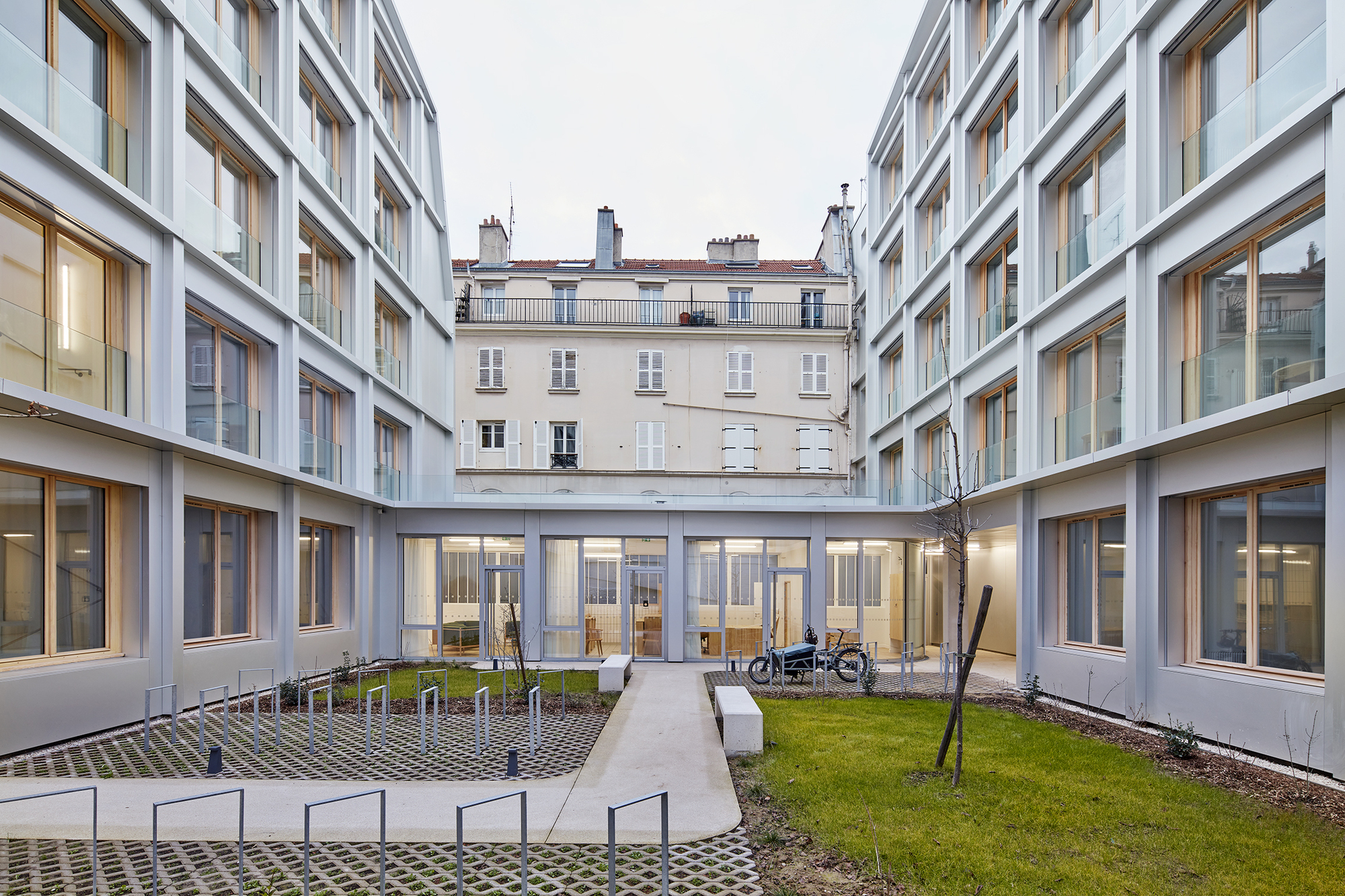 Courtyard view at dusk with glazed ground floor passage connecting two wings and bicycles parked outside