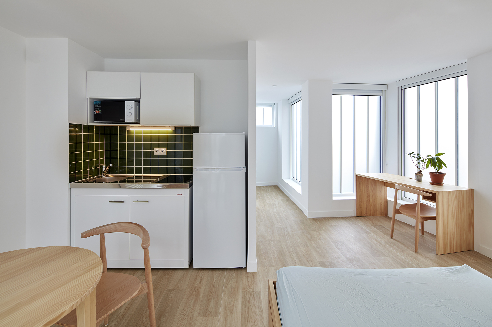 Studio unit with kitchenette featuring dark green tile backsplash and light wood flooring throughout