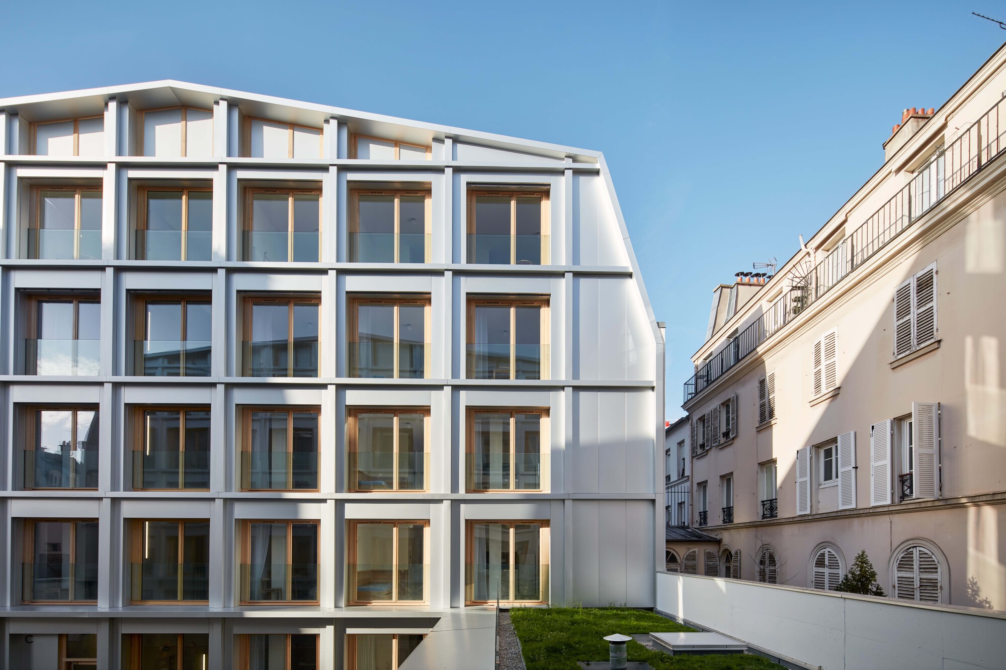 Street facade with curved mansard roofline and white structural grid adjacent to neighboring residential buildings