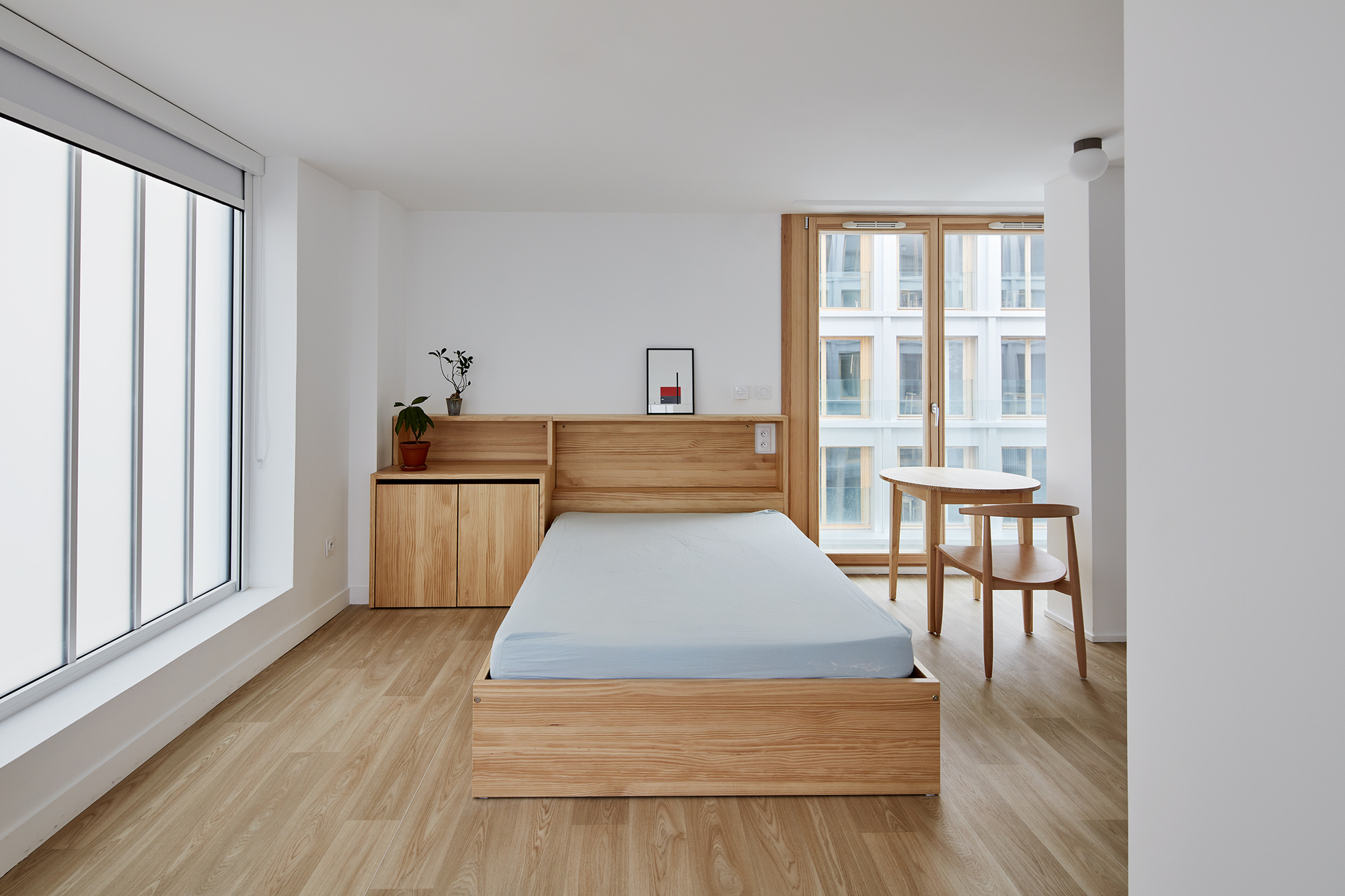 Bedroom with timber platform bed and built-in headboard storage overlooking the courtyard through large windows