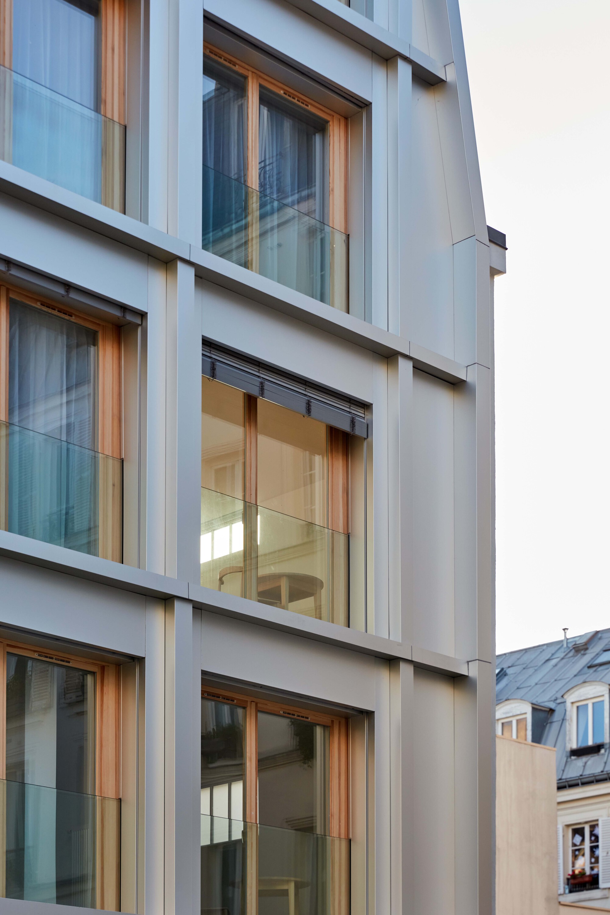 Close-up of white concrete panels and timber window frames with glass balustrades under overcast sky
