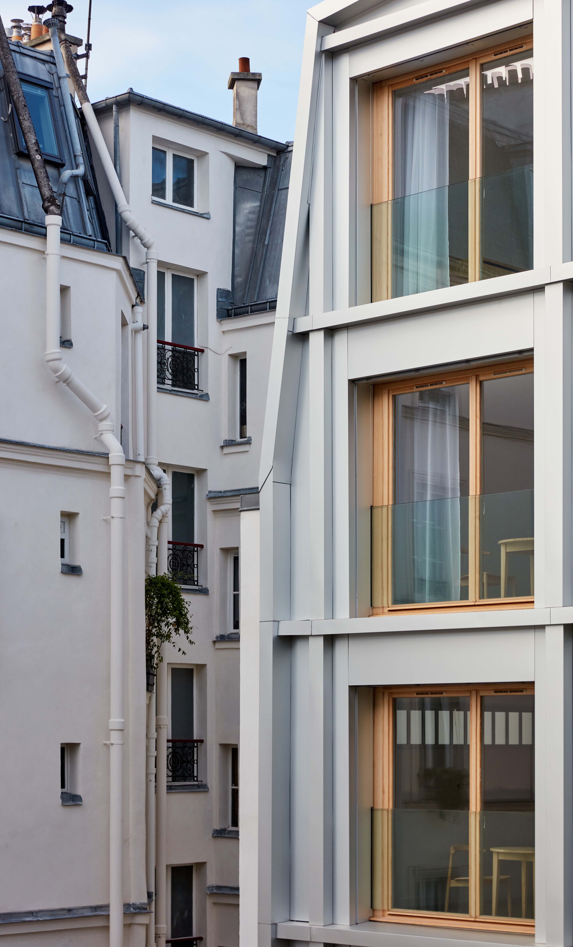 Rear elevation with recessed timber windows nestled between neighboring masonry buildings at twilight