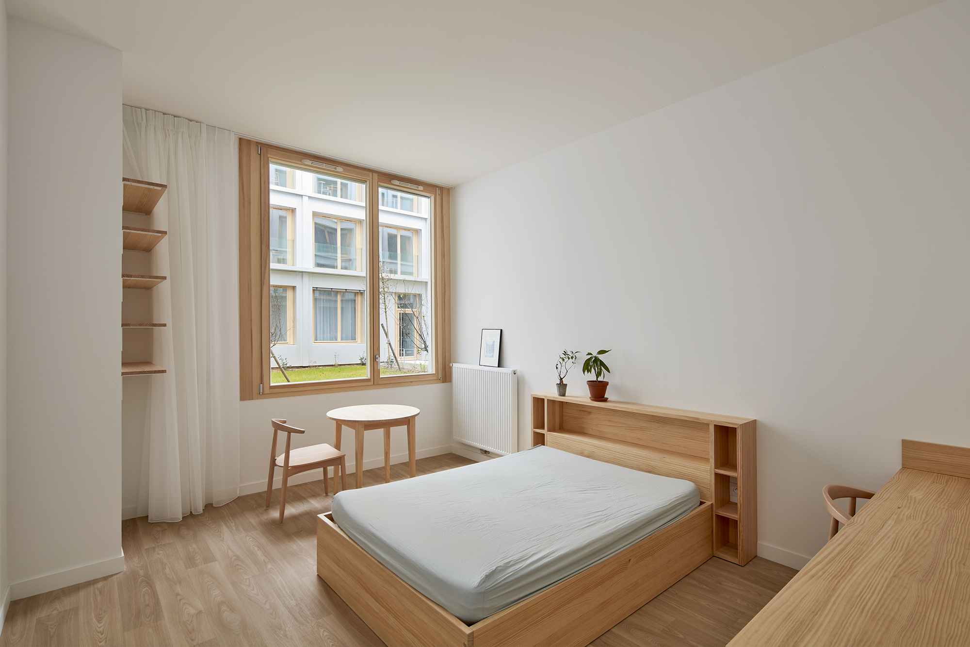 Bedroom with timber bed frame and open shelving beside a timber-framed window overlooking a courtyard