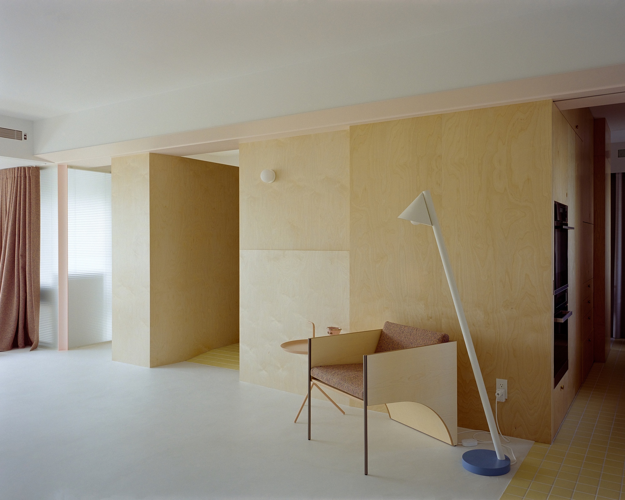 Interior with freestanding plywood volumes and a pale blue floor lamp beside a timber chair