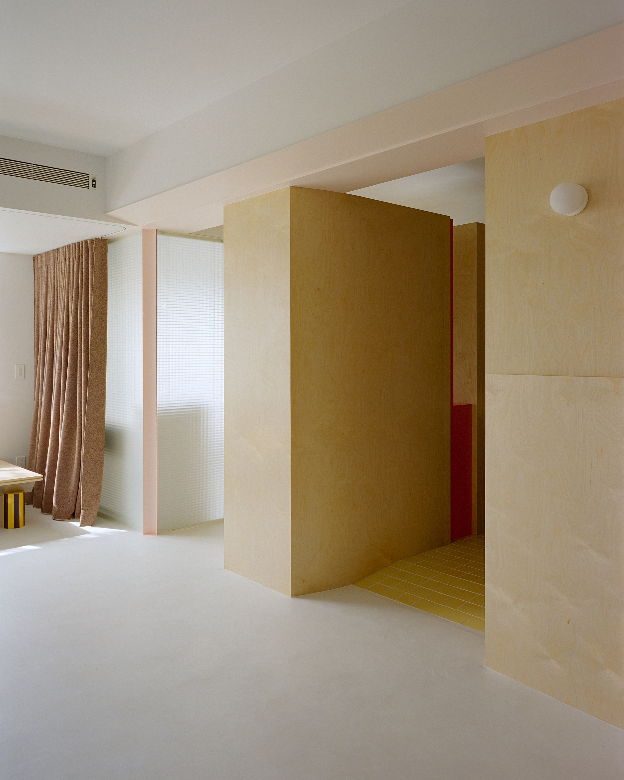 Threshold between white floor and yellow tiled floor framed by plywood walls and red accent