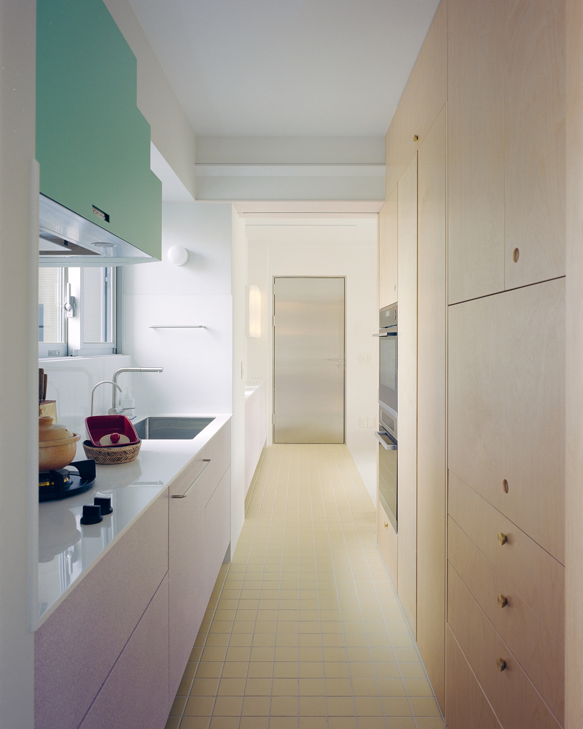 Galley kitchen with mint green hood and plywood cabinetry along yellow tiled floor