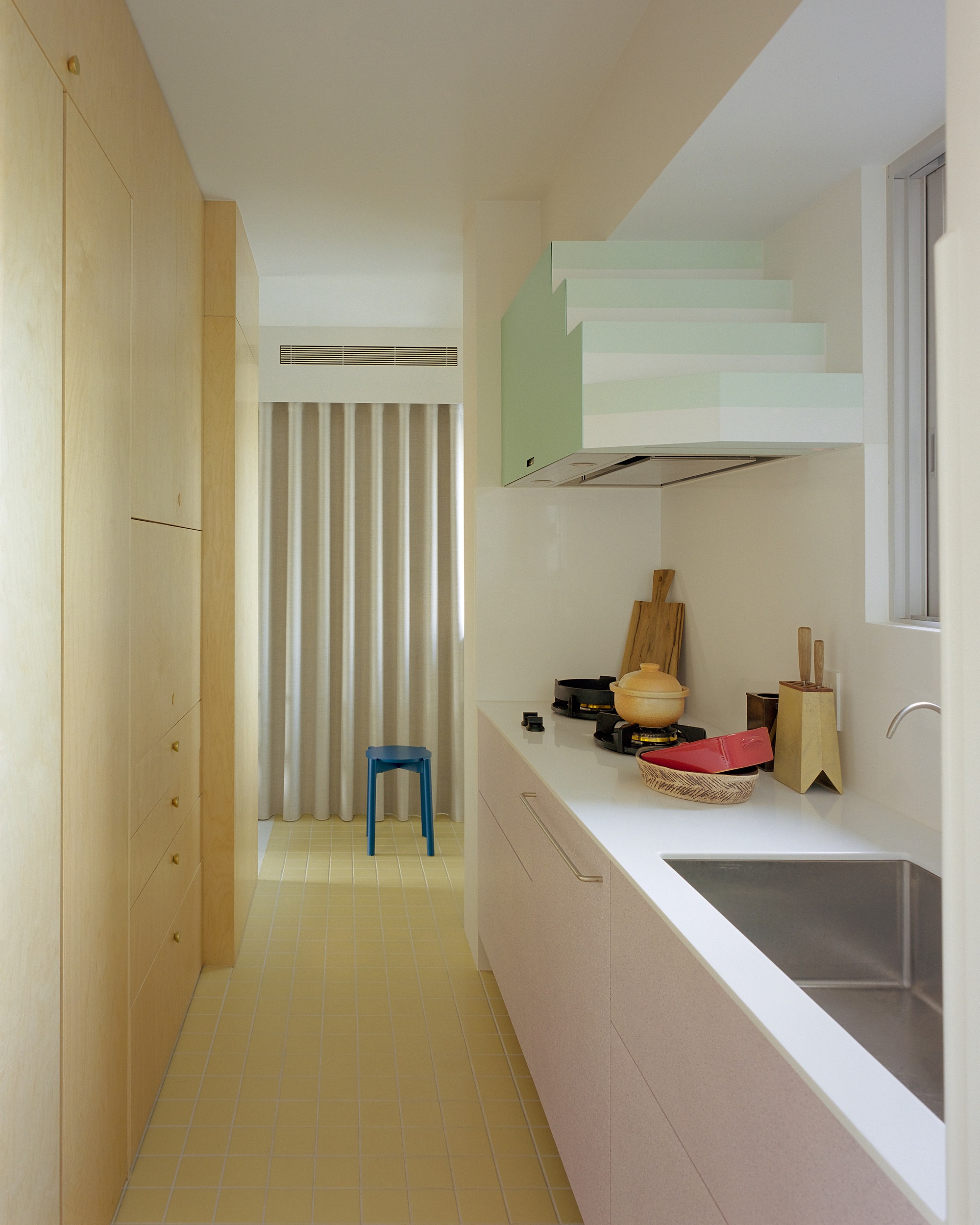 Kitchen counter with sink and pale green range hood beyond a vertical slatted screen