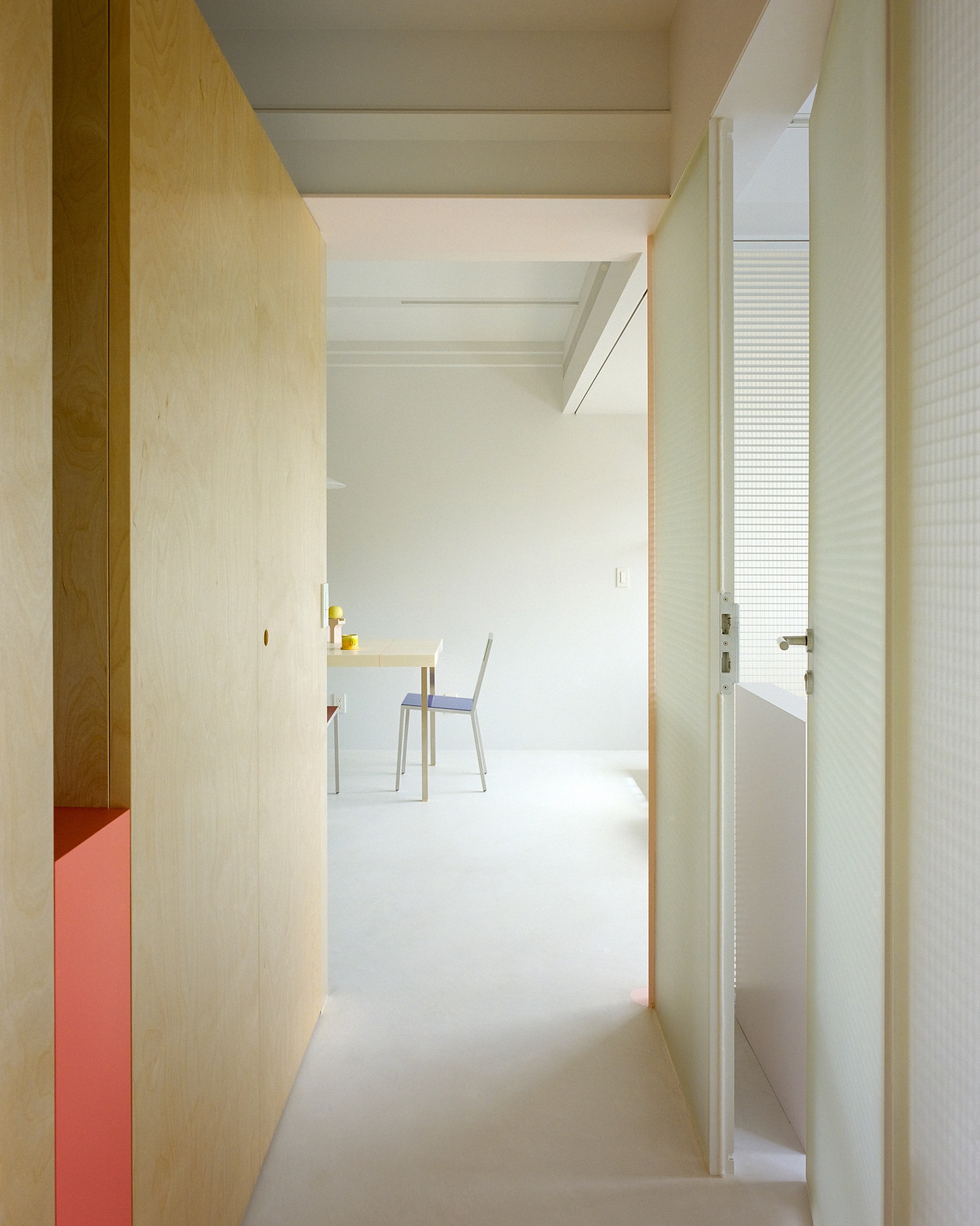 Narrow corridor with light plywood walls and white ceiling beams leading to a dining area