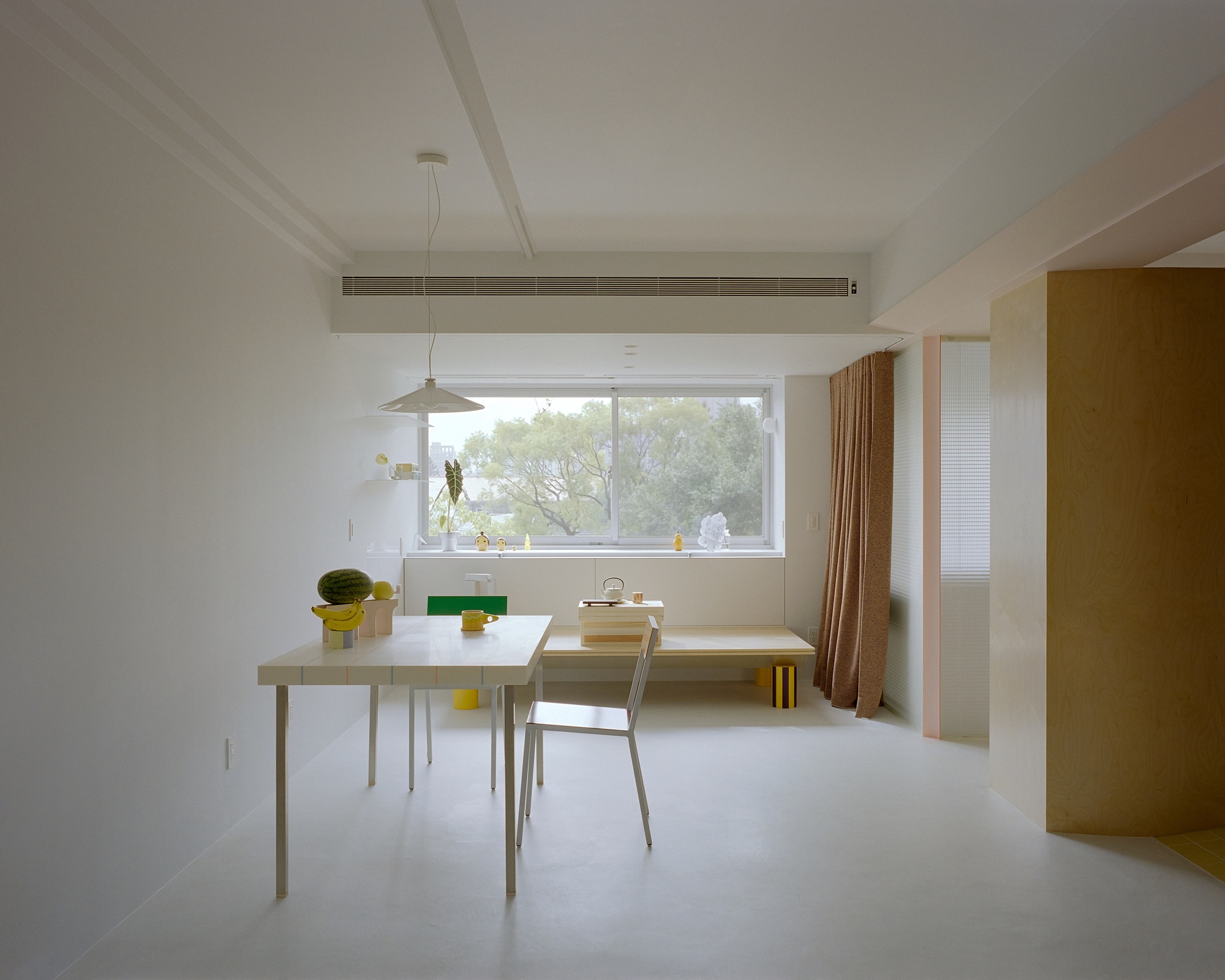 Dining area with pendant light, horizontal window framing green foliage and brown curtain at right