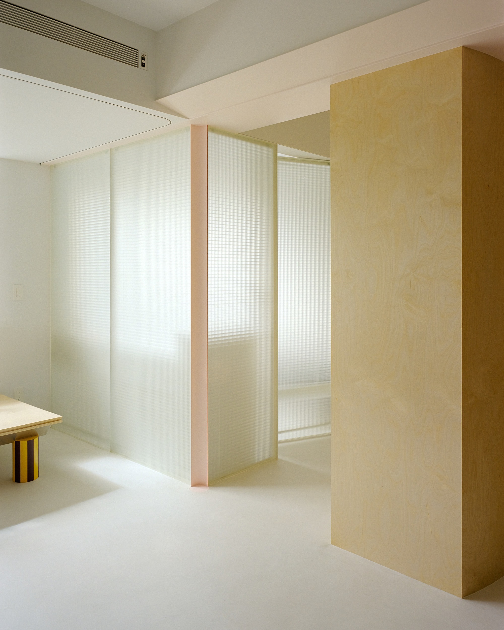 Translucent pleated partition panels framed in pale wood dividing the white interior