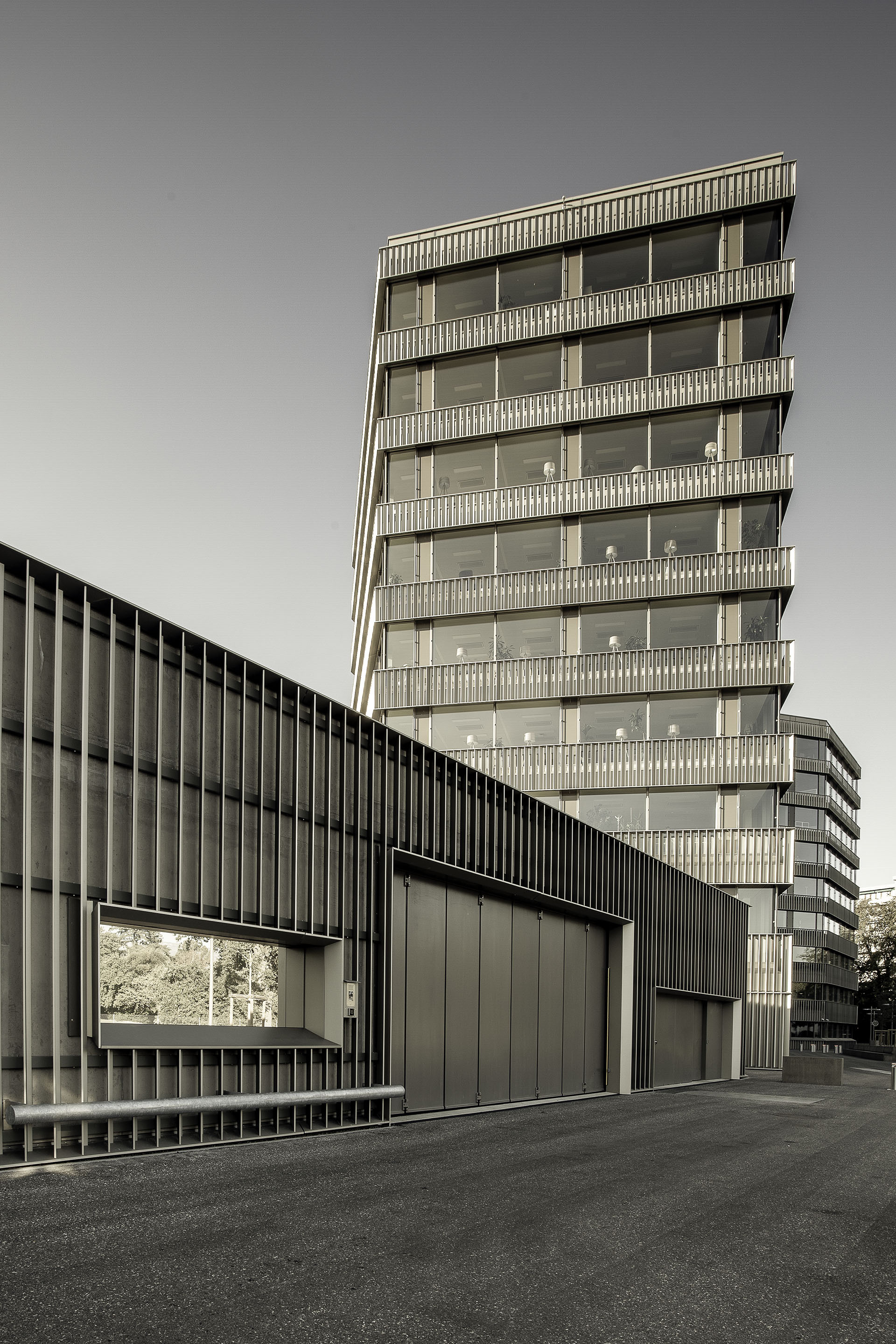 Vertical louvered tower behind a dark ribbed garage volume with metal gates
