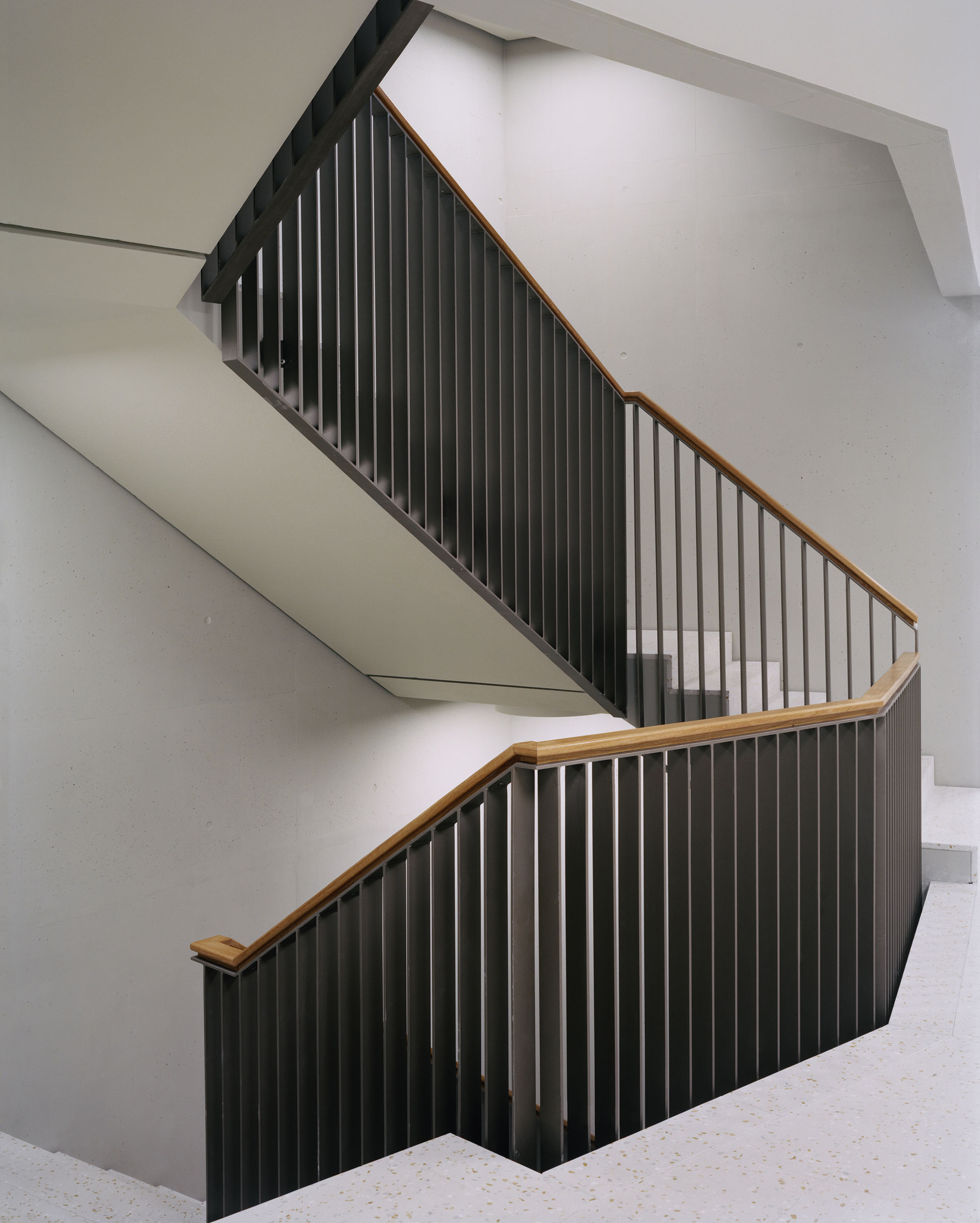 Switchback staircase with vertical black metal balustrades and timber handrails against white walls