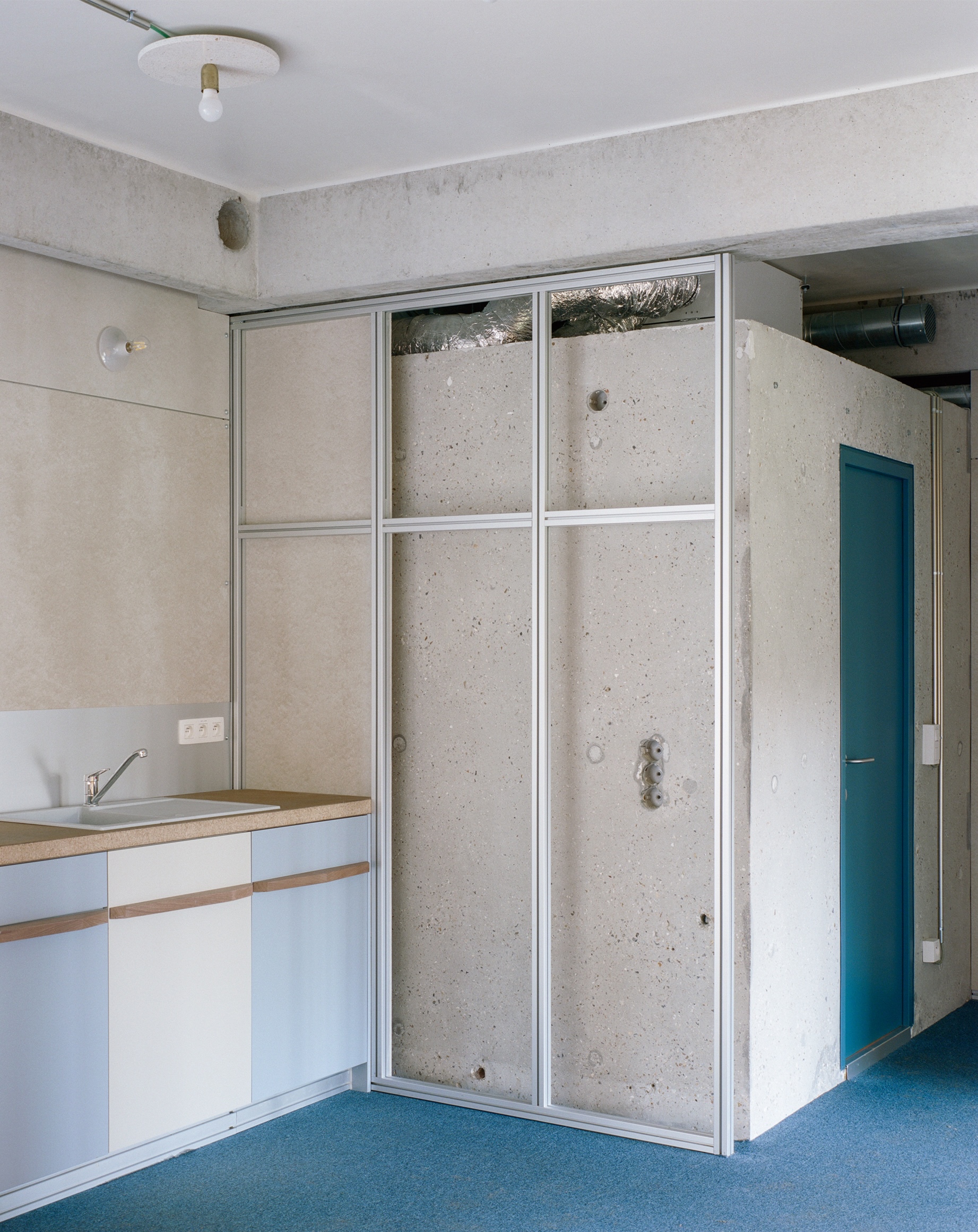 Kitchen with white countertop and tall concrete panels framed by white metal mullions near blue door