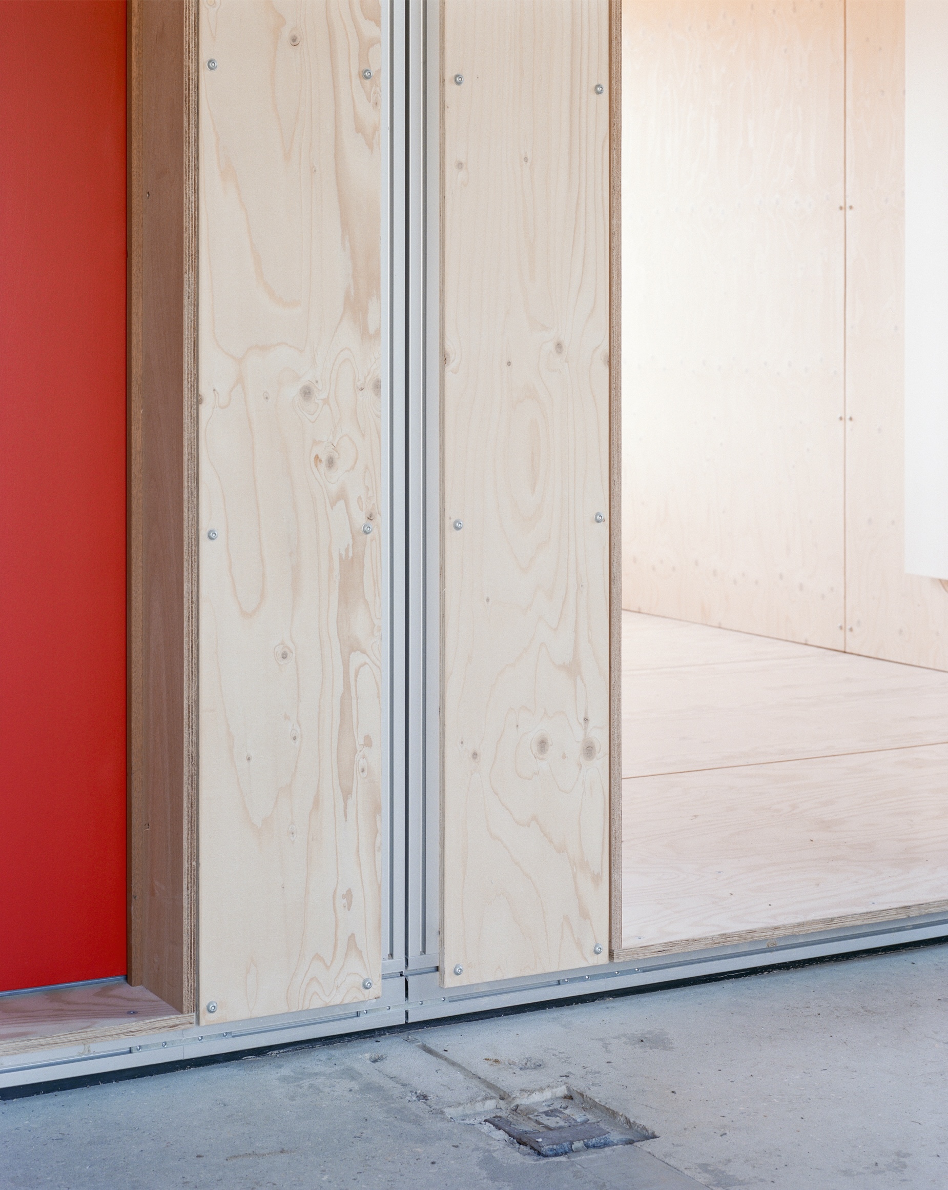 Detail of plywood door frame with exposed screws meeting grey concrete floor