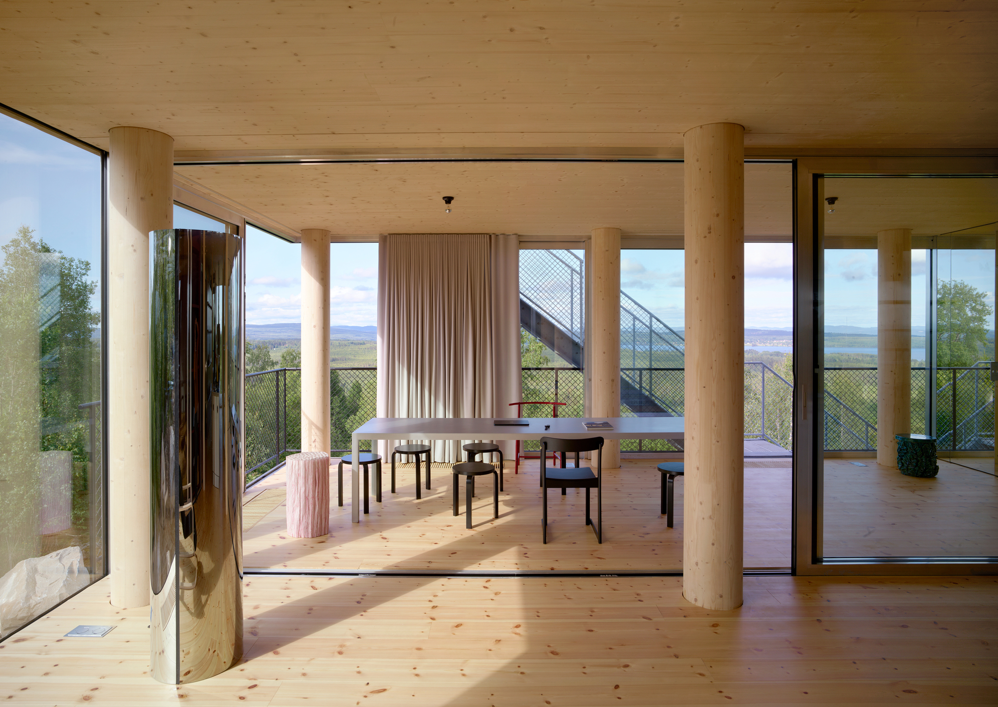 Interior dining space with pale timber columns and plywood ceiling framing views of hills and lake