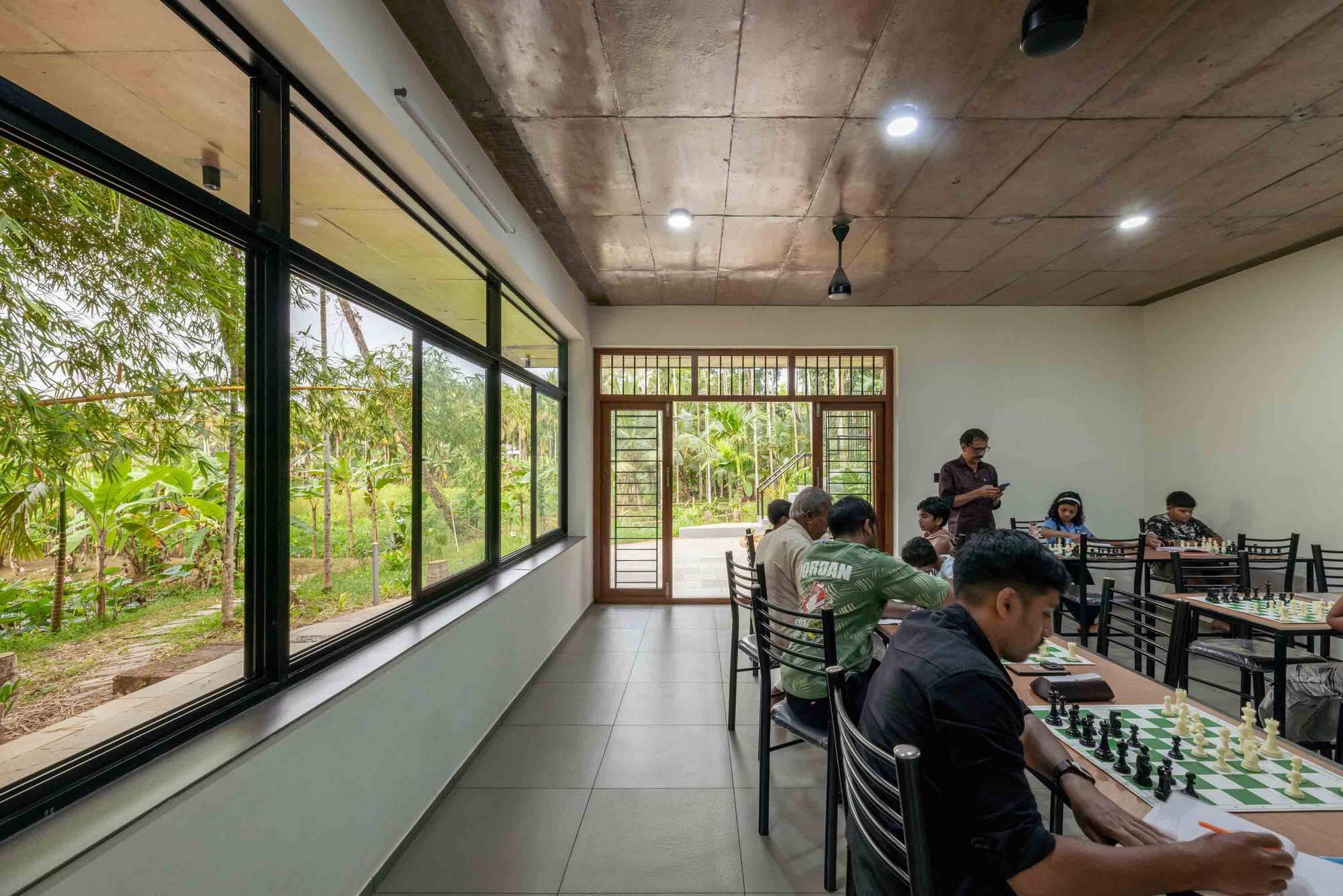Long room with exposed concrete ceiling and continuous glazing opening to the wooded landscape beyond