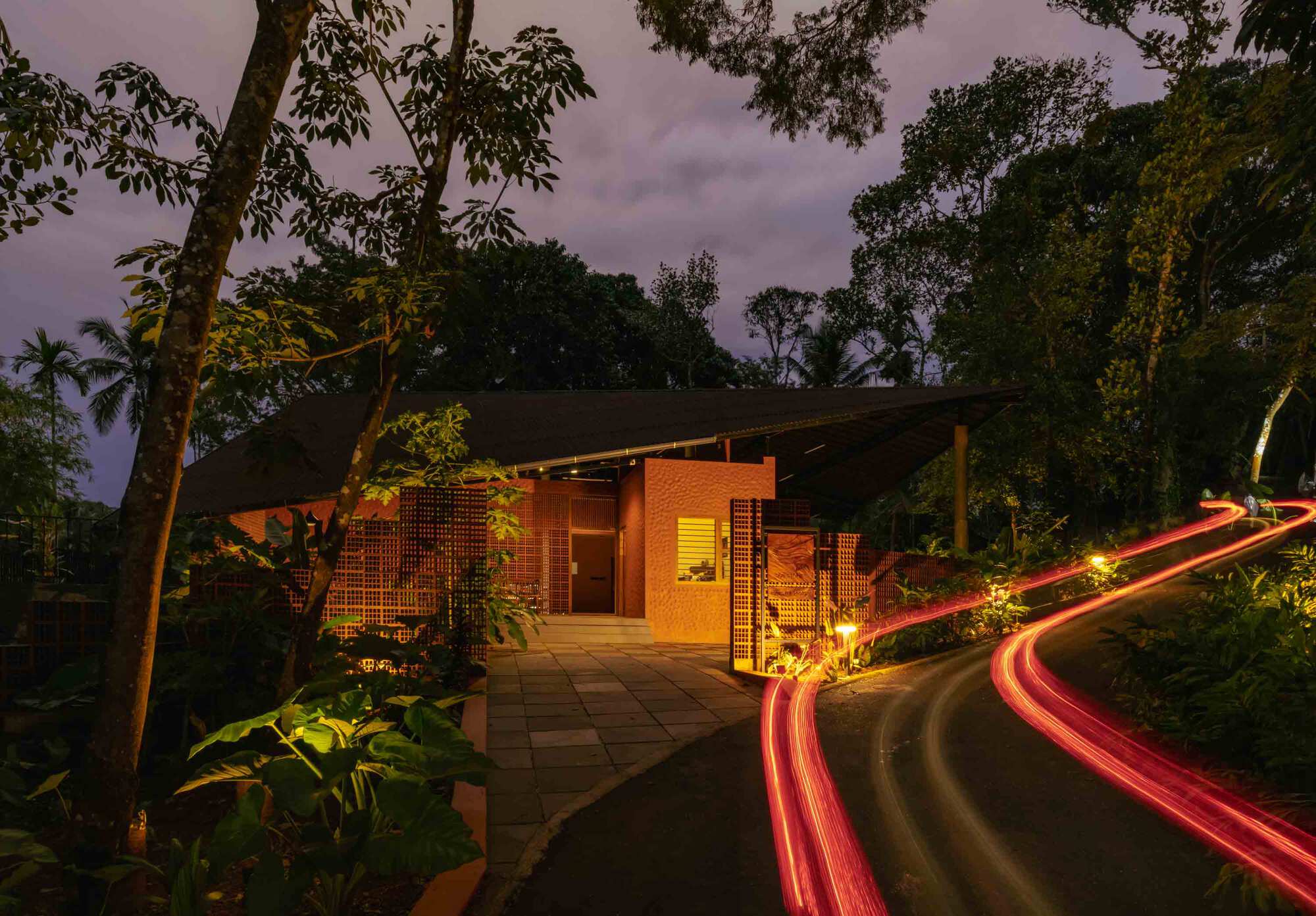 Long exposure at dusk showing vehicle light trails along the entry drive and illuminated brick screens
