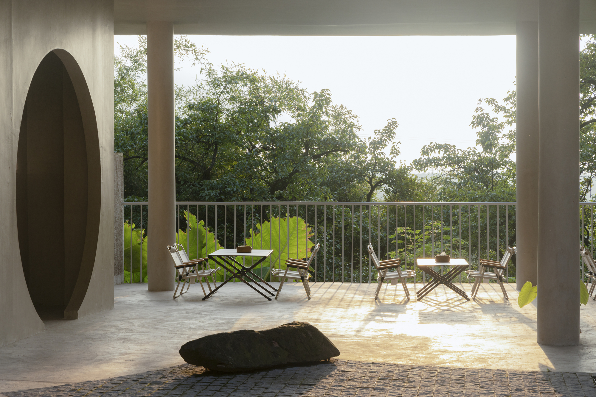 Covered terrace with cylindrical columns and metal railings framing outdoor furniture and tropical vegetation