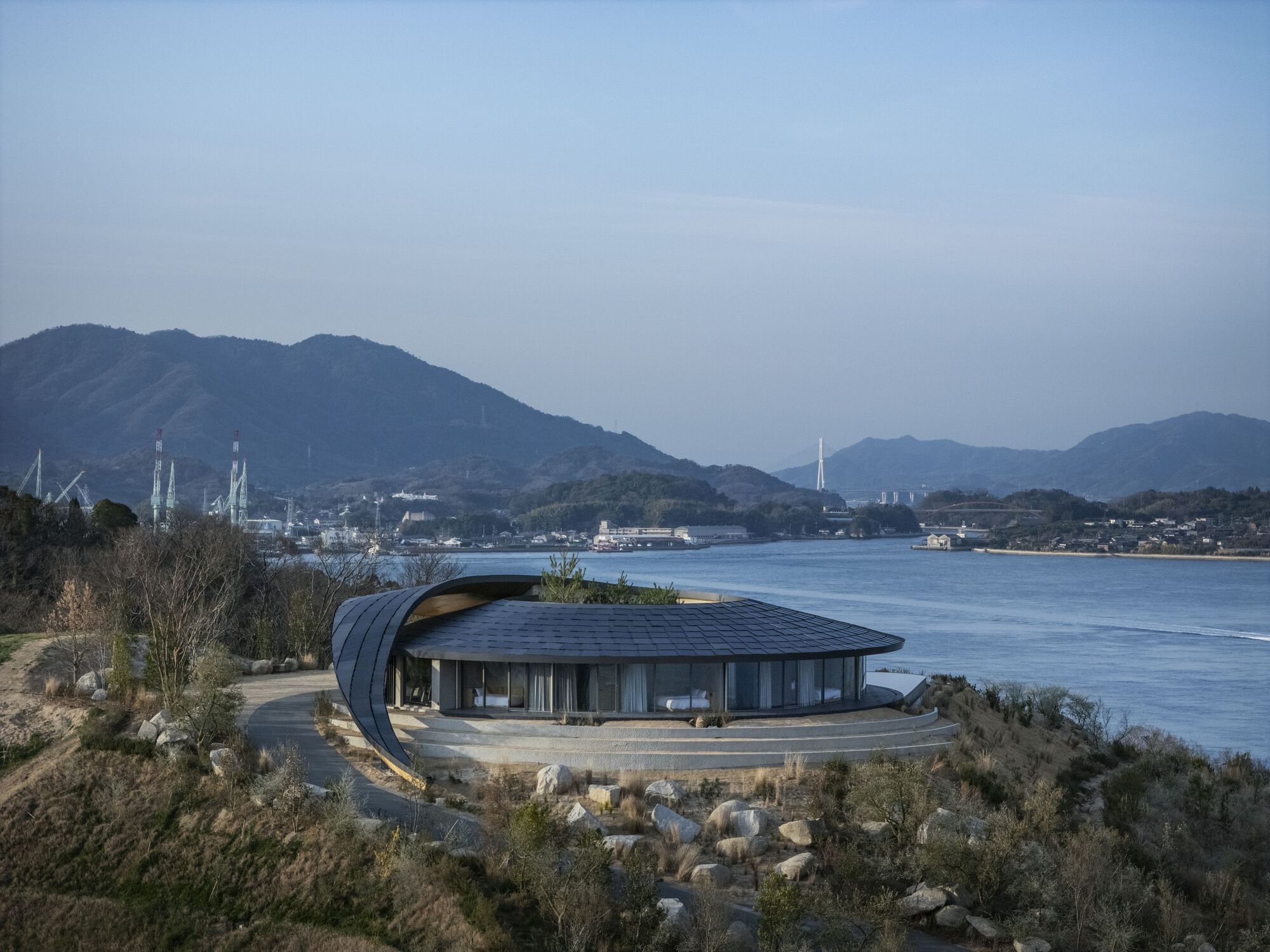 Side view of the glass-walled pavilion with its sweeping roof form overlooking the calm water
