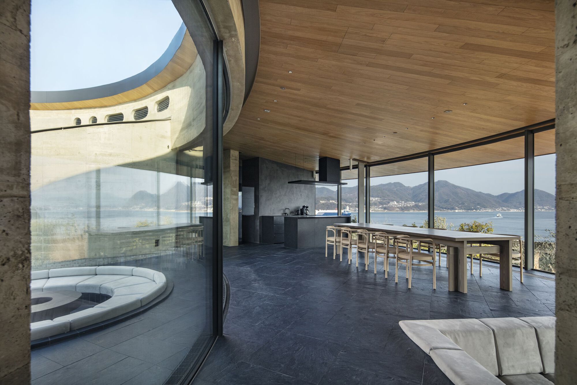 Interior dining area with timber ceiling, dark stone floor and glazed walls opening to the waterfront