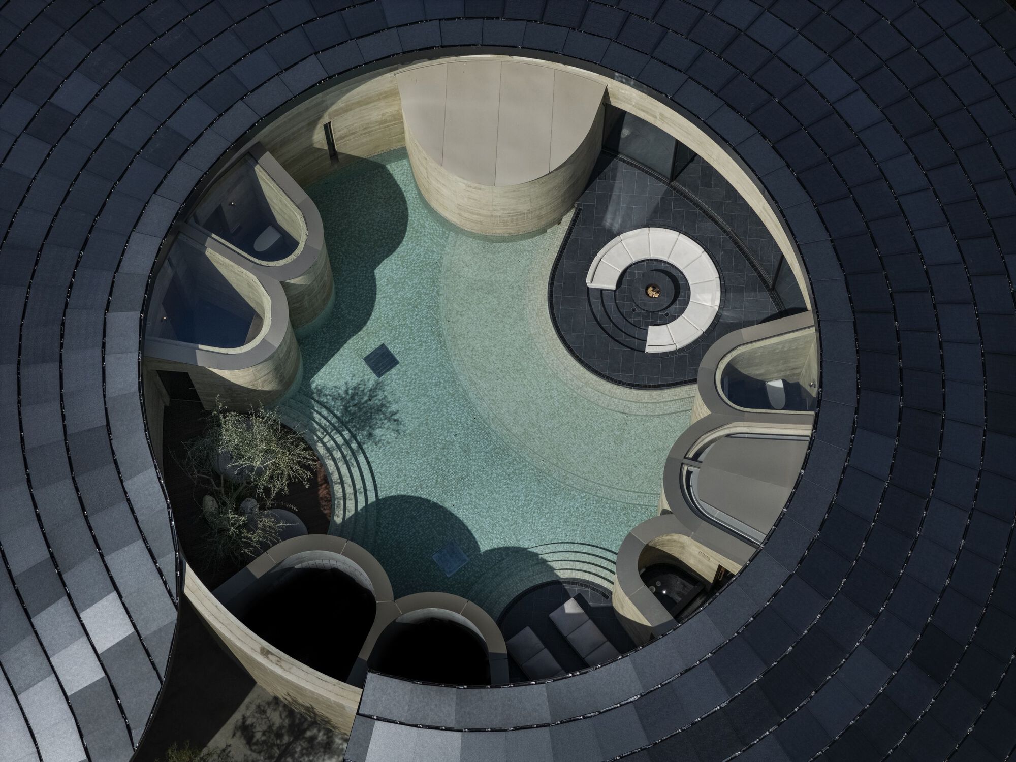 Top-down view through a circular roof opening revealing a pool and curved lounge platforms below