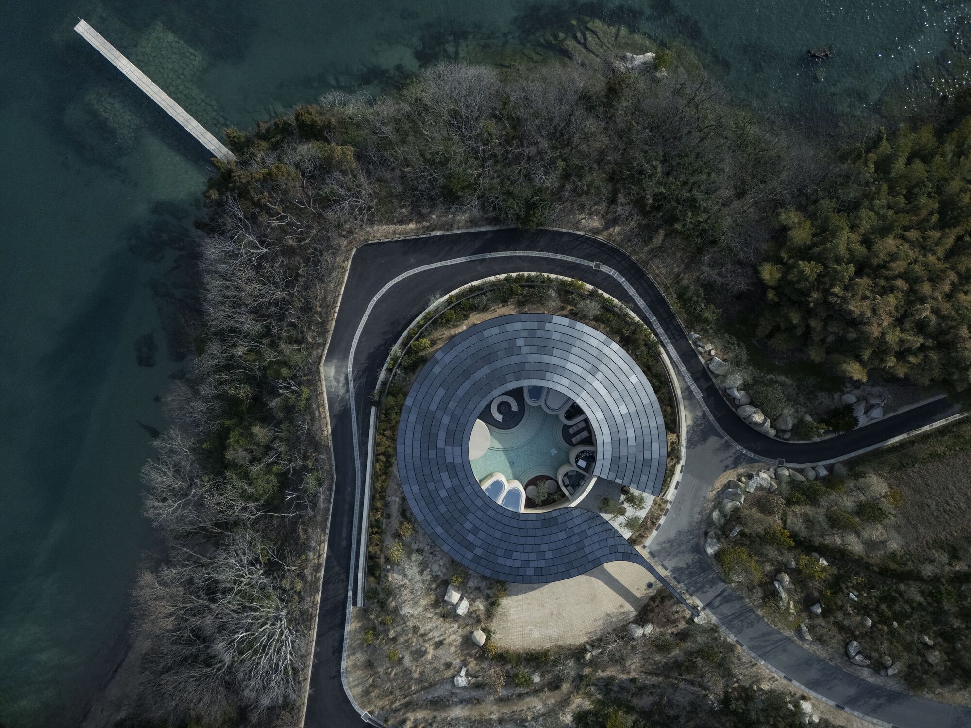 Aerial view of the circular roof with central oculus surrounded by planted terrace and lake water