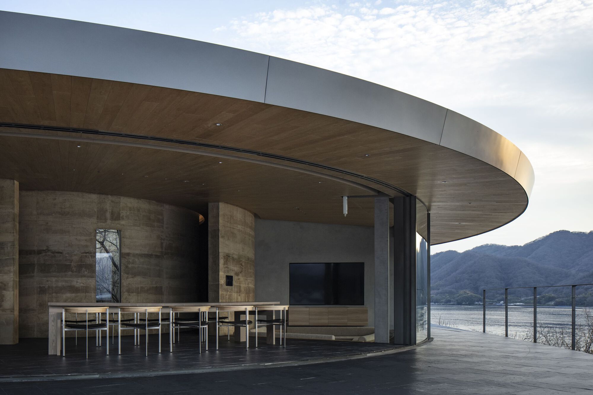 Covered terrace with overhanging disc roof, timber ceiling soffit and dining table facing the lake