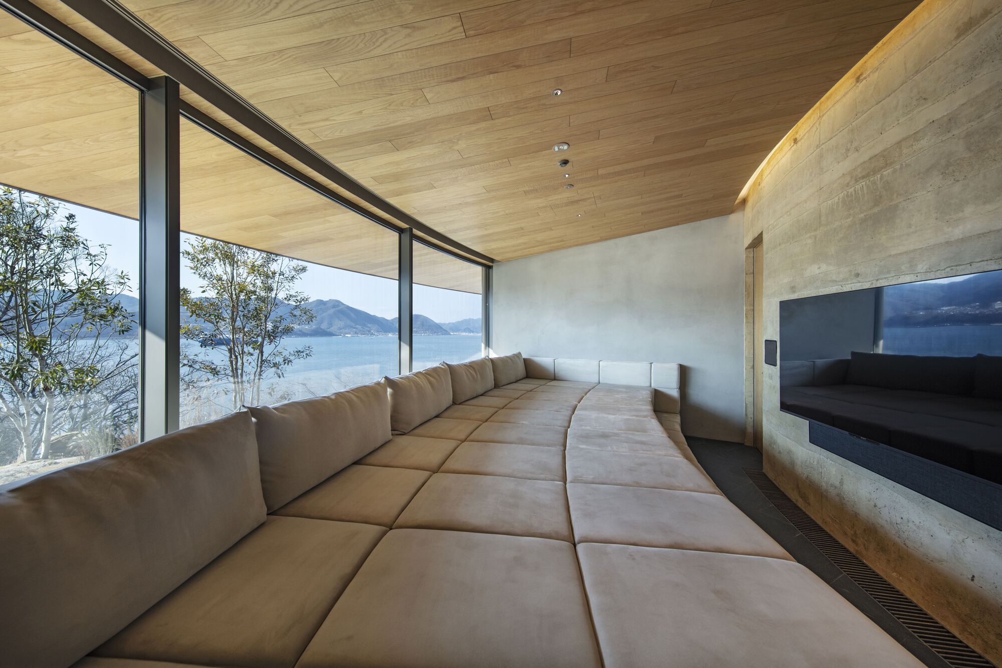 Curved lounge area with upholstered seating, concrete walls and continuous glazing framing the lake view