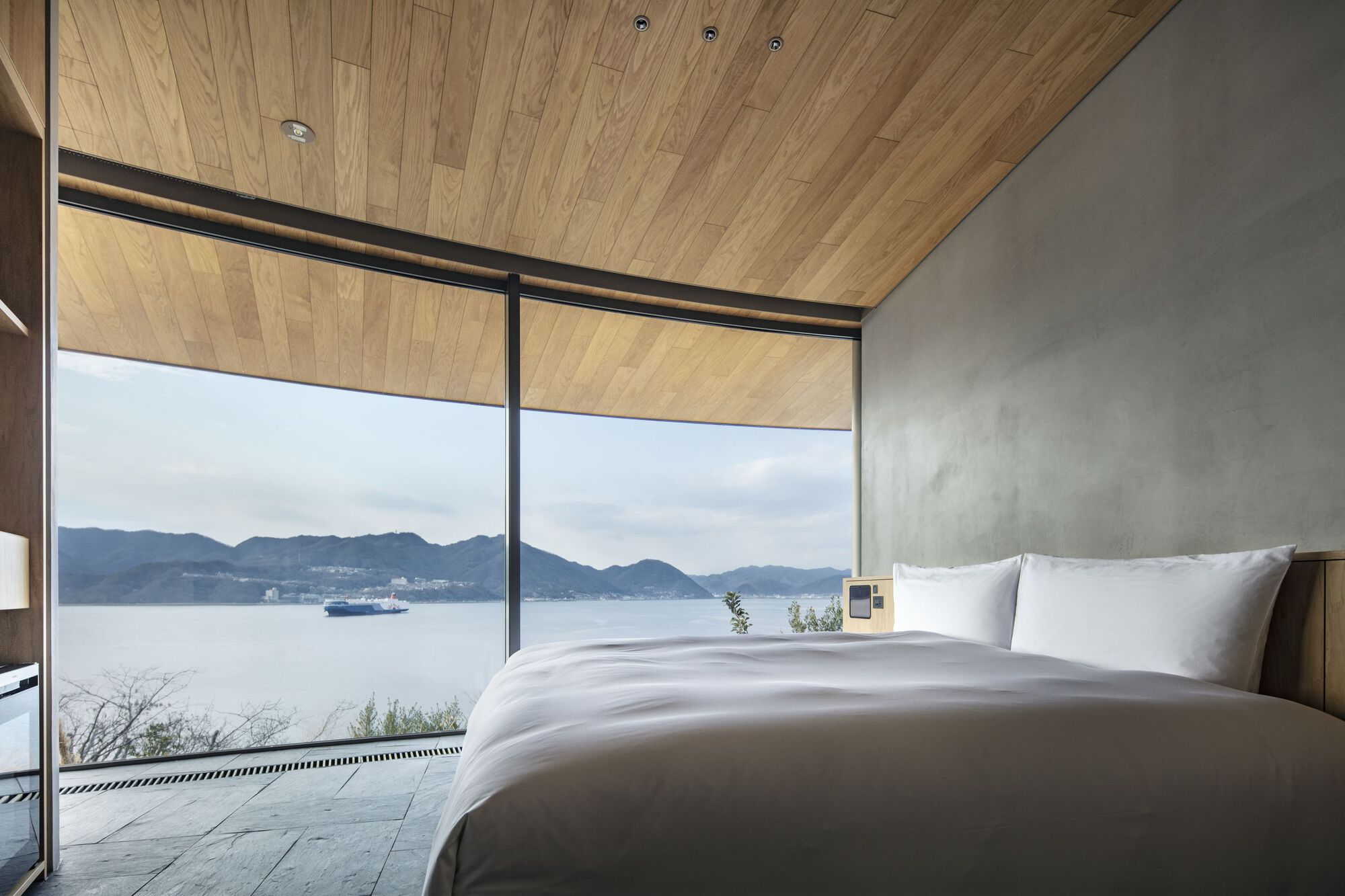 Bedroom with timber plank ceiling overlooking the lake and distant mountains under overcast skies